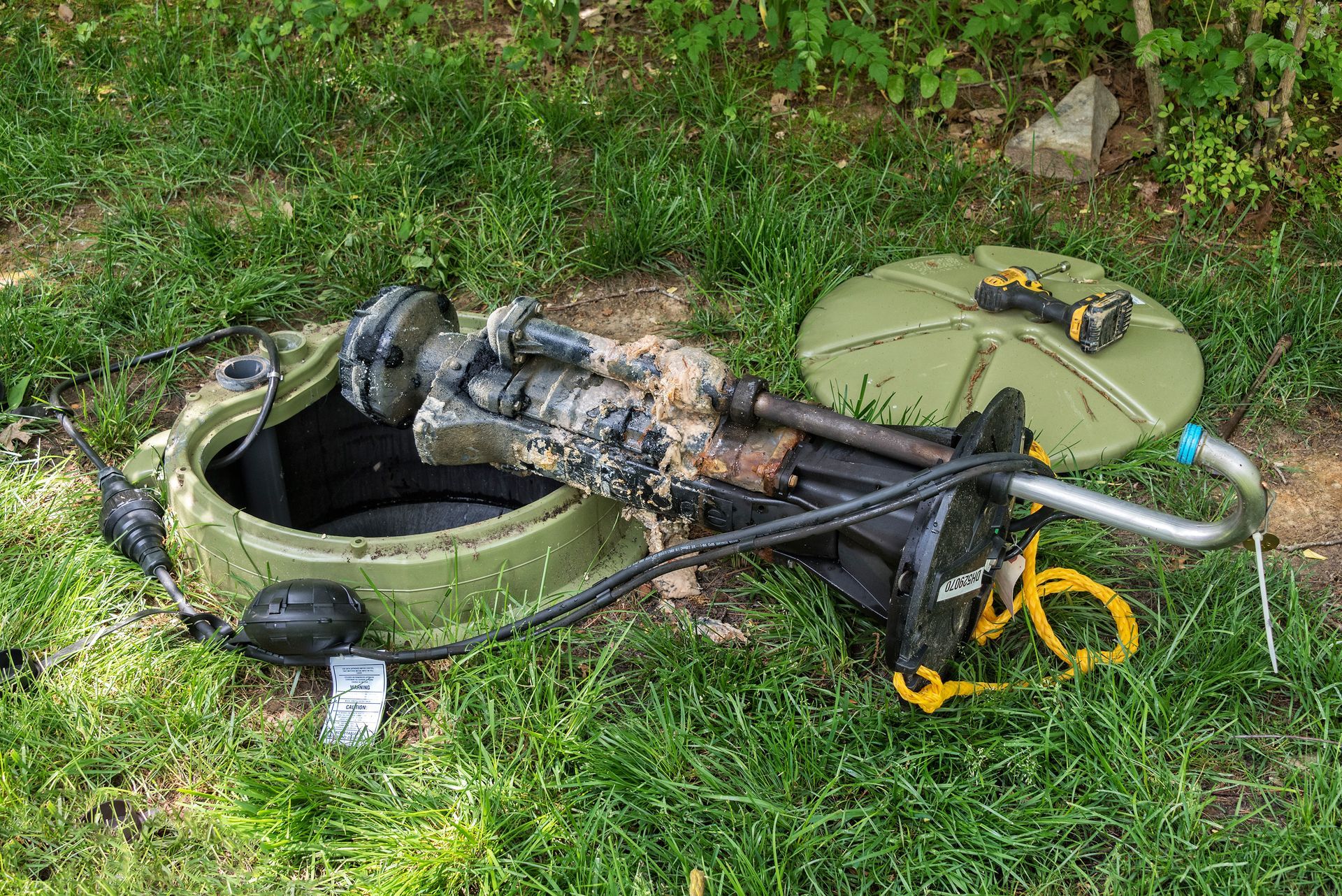 Broken scooter and parts lying in grass beside an open manhole cover.