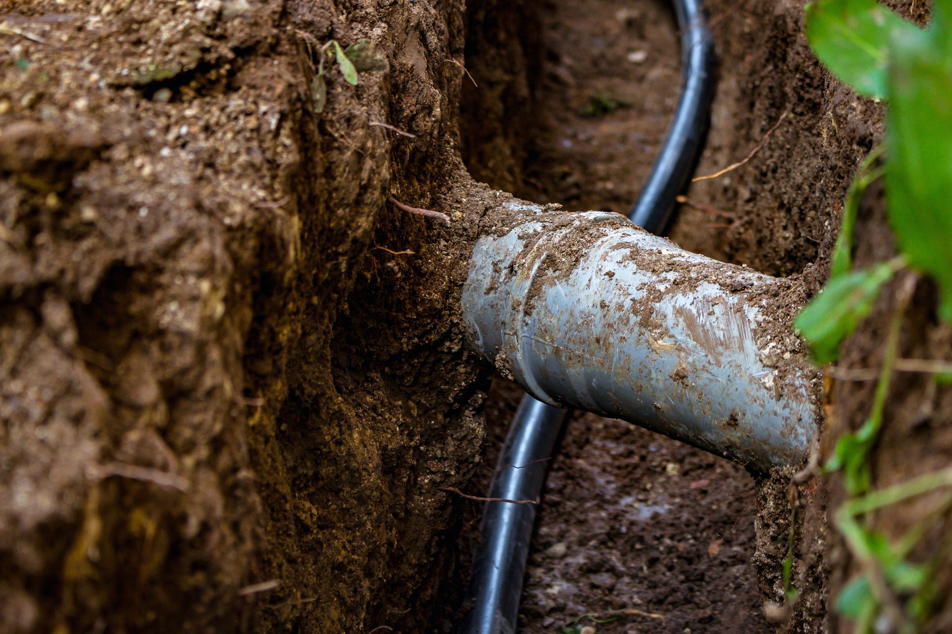 Rusty metal pipe emerging from a dirt trench beside a black cable.