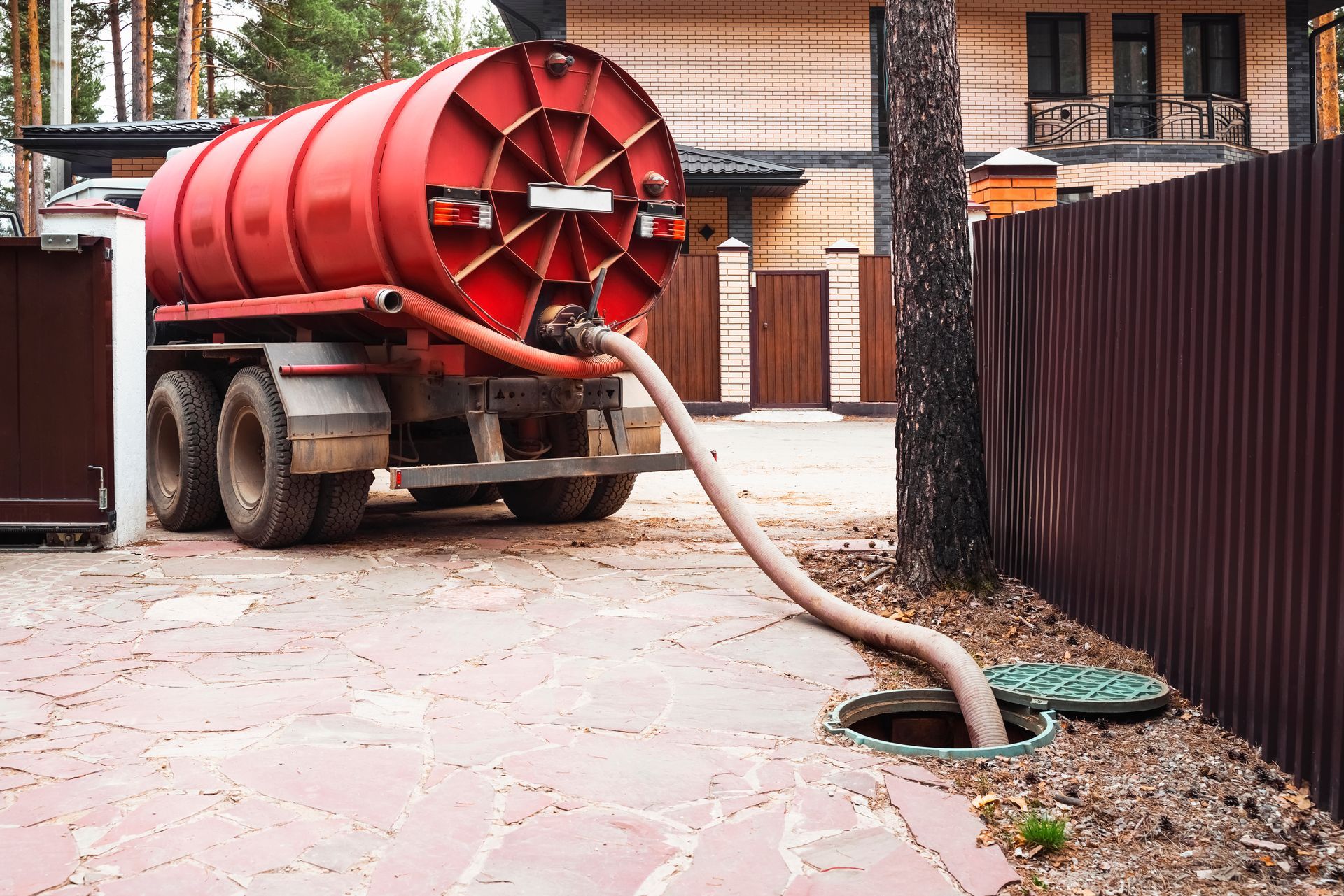 Red vacuum truck with a hose cleaning a courtyard driveway near an apartment building