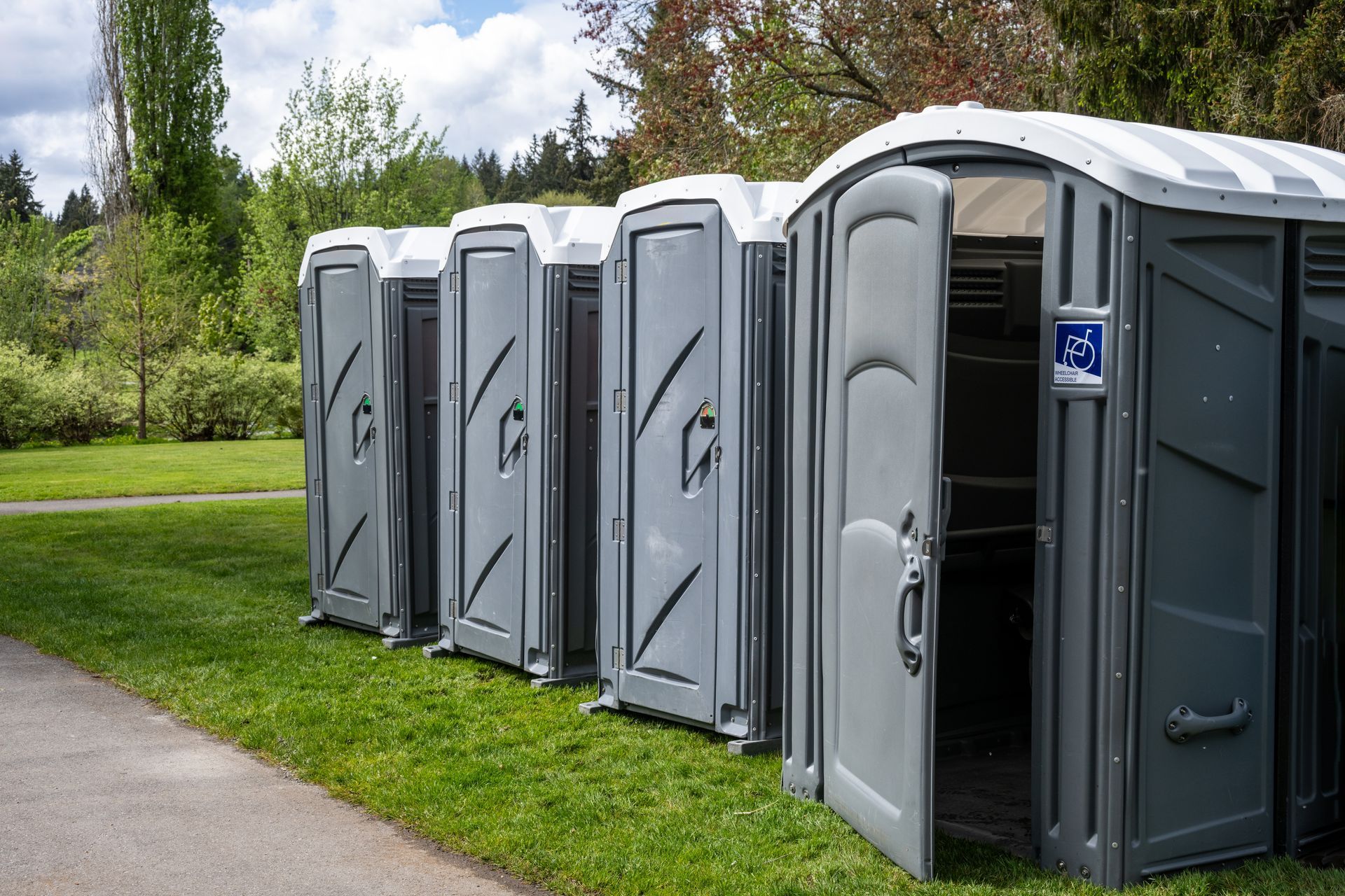 Row of gray portable toilets along a grassy path in a park