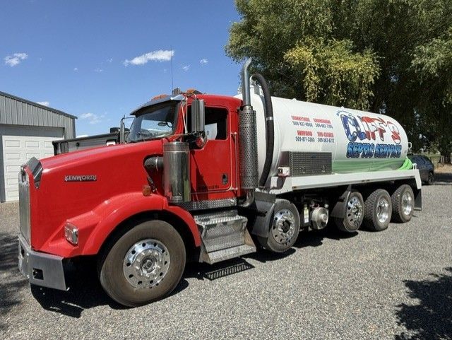 Orange tanker truck with workers on a wet street outside a brick building