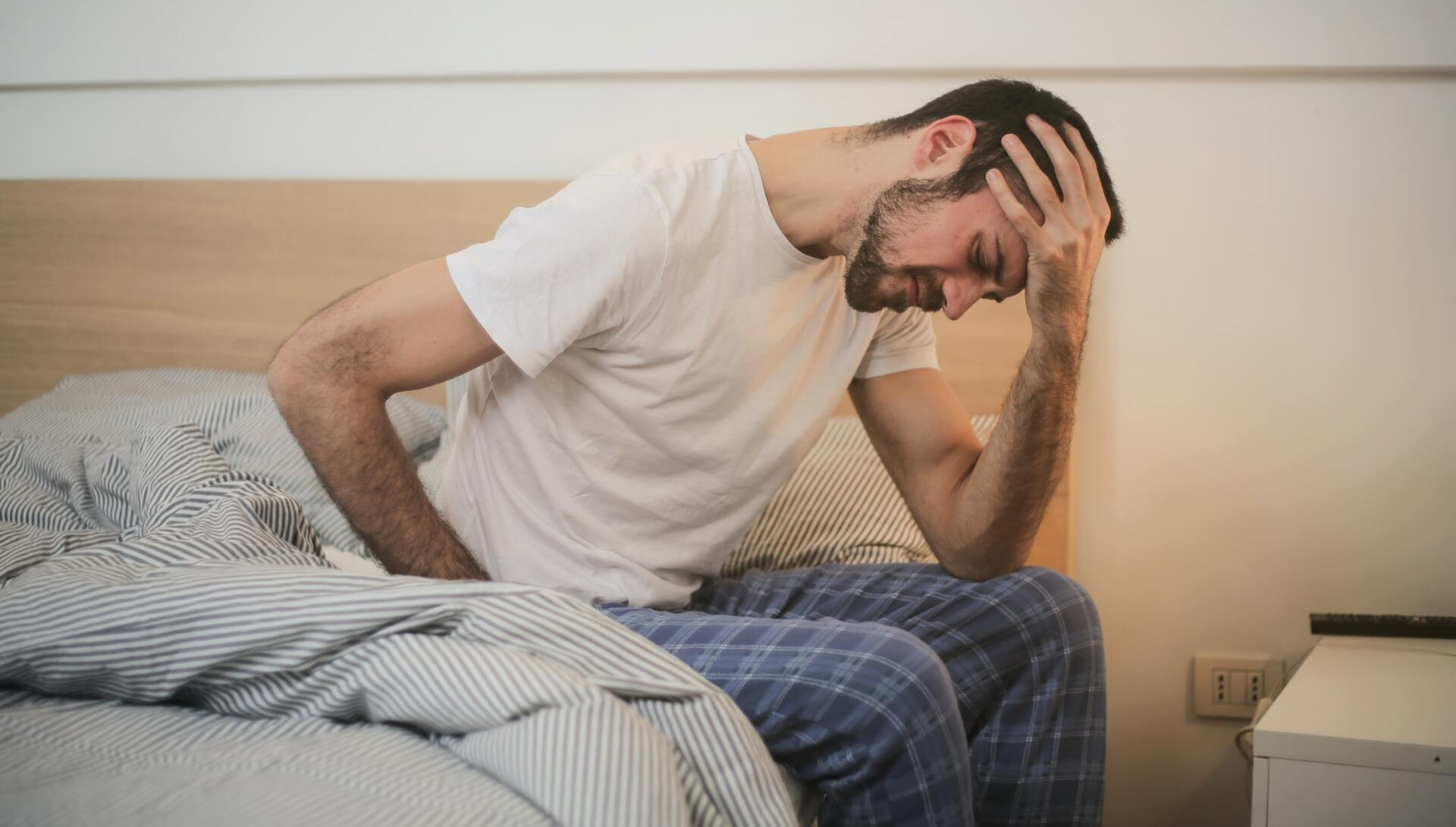 A man is sitting on a bed holding his stomach in pain.