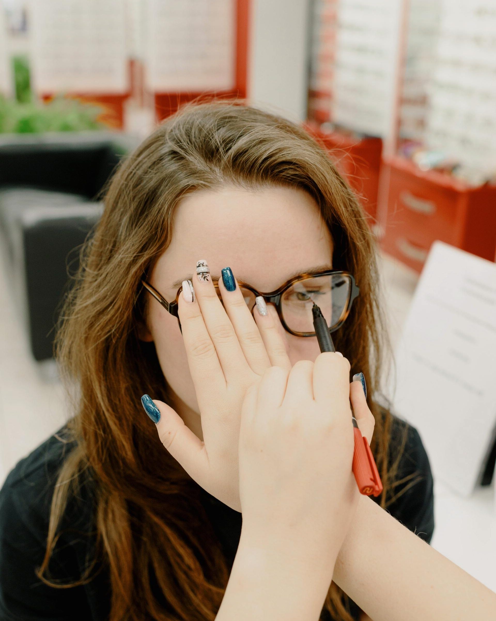 A woman wearing glasses is covering her face with her hands