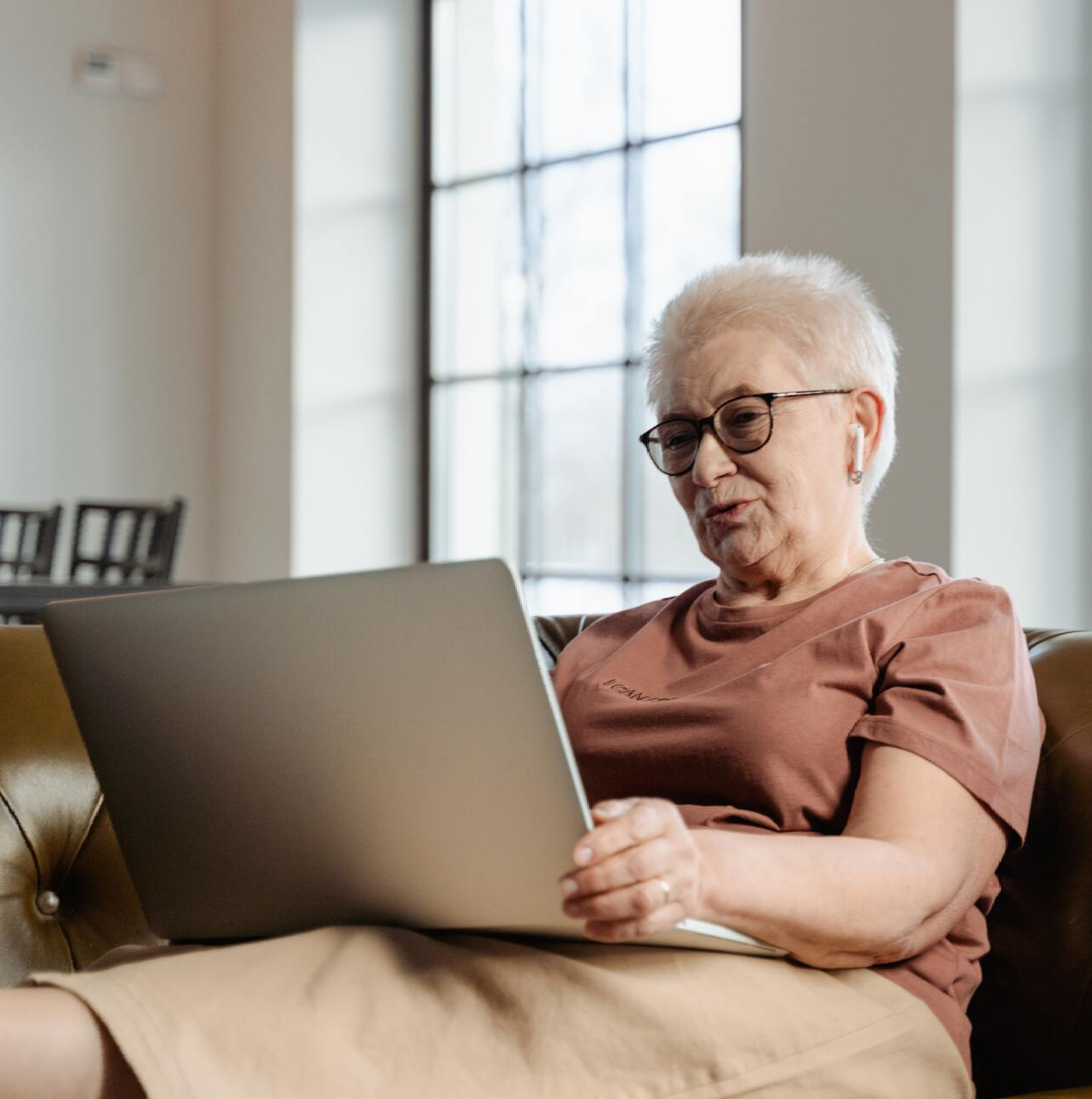An elderly woman is sitting on a couch using a laptop computer.