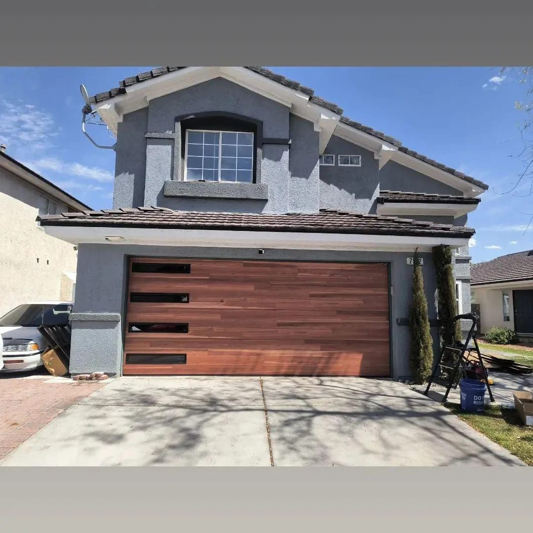A car is parked in front of a house with a wooden garage door.
