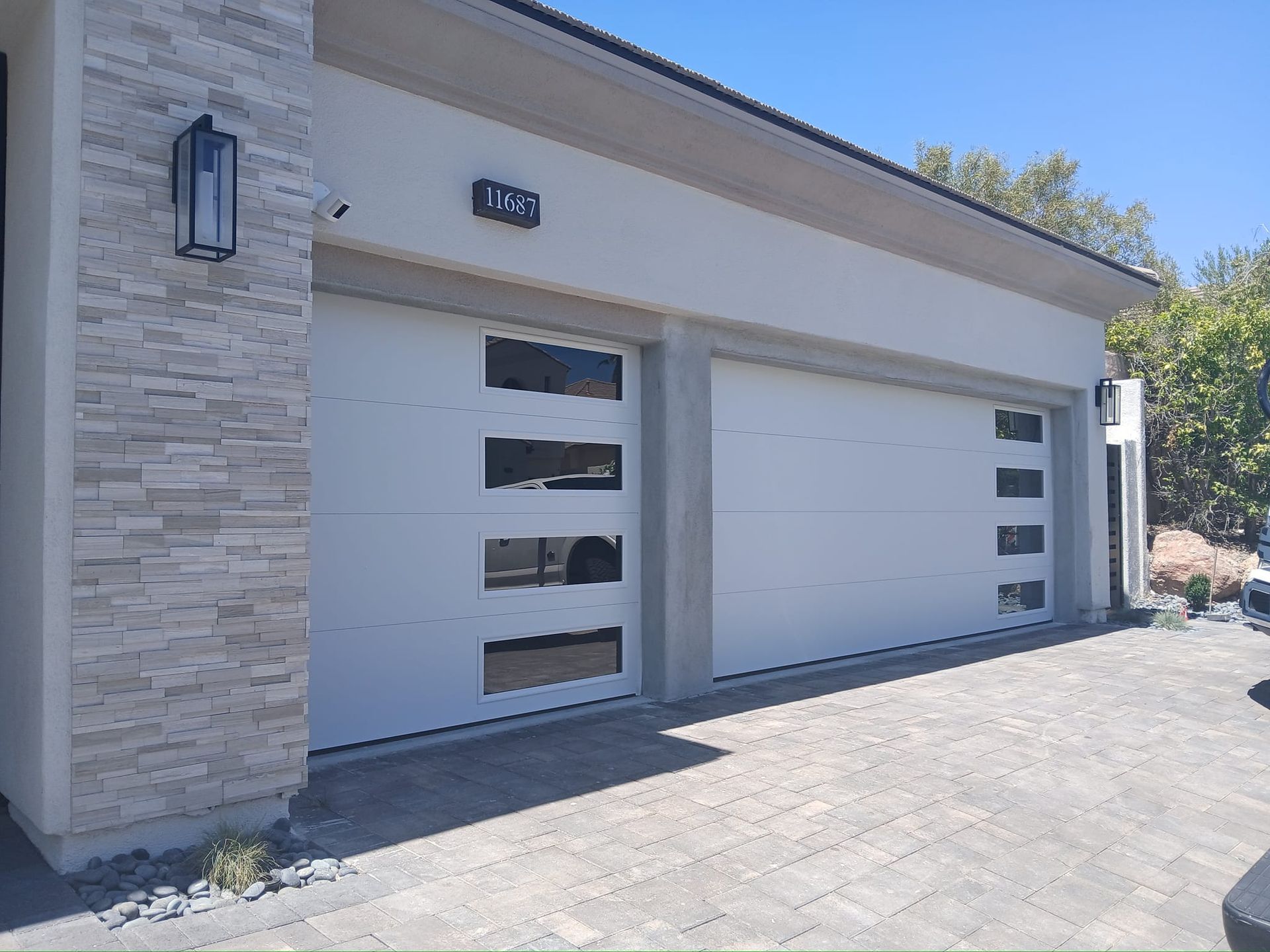 A white garage door with a brick wall and a car parked in front of it.