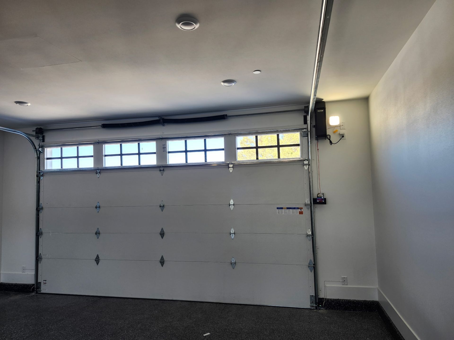 An empty garage with a garage door open and a light on the ceiling.