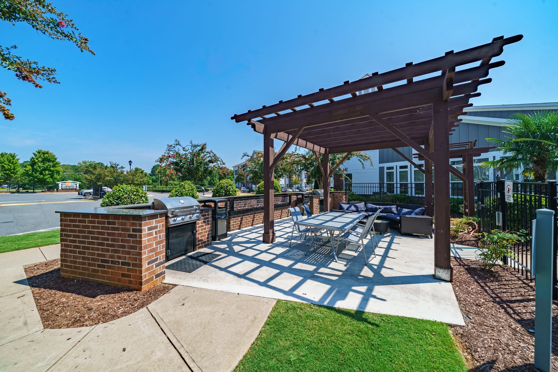 Covered outdoor picnic area with wooden pergola, tables, brick grill, and sunny park setting at Willows at Fort Mill apartments for rent in SC.