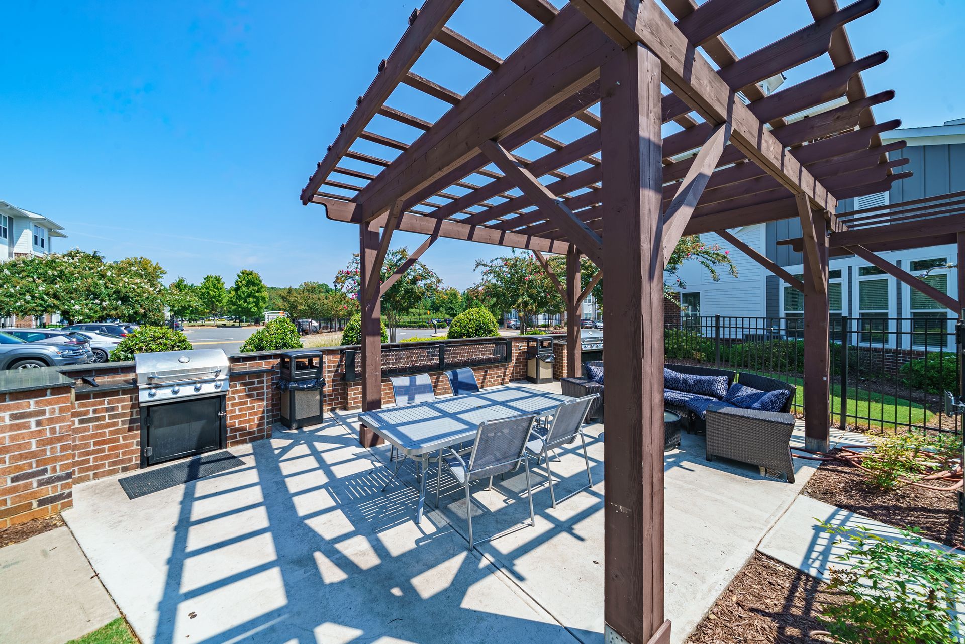 Outdoor patio with pergola, dining table, and brick grilling area beside a pool under a blue sky at Willows at Fort Mill apartments for rent in SC.