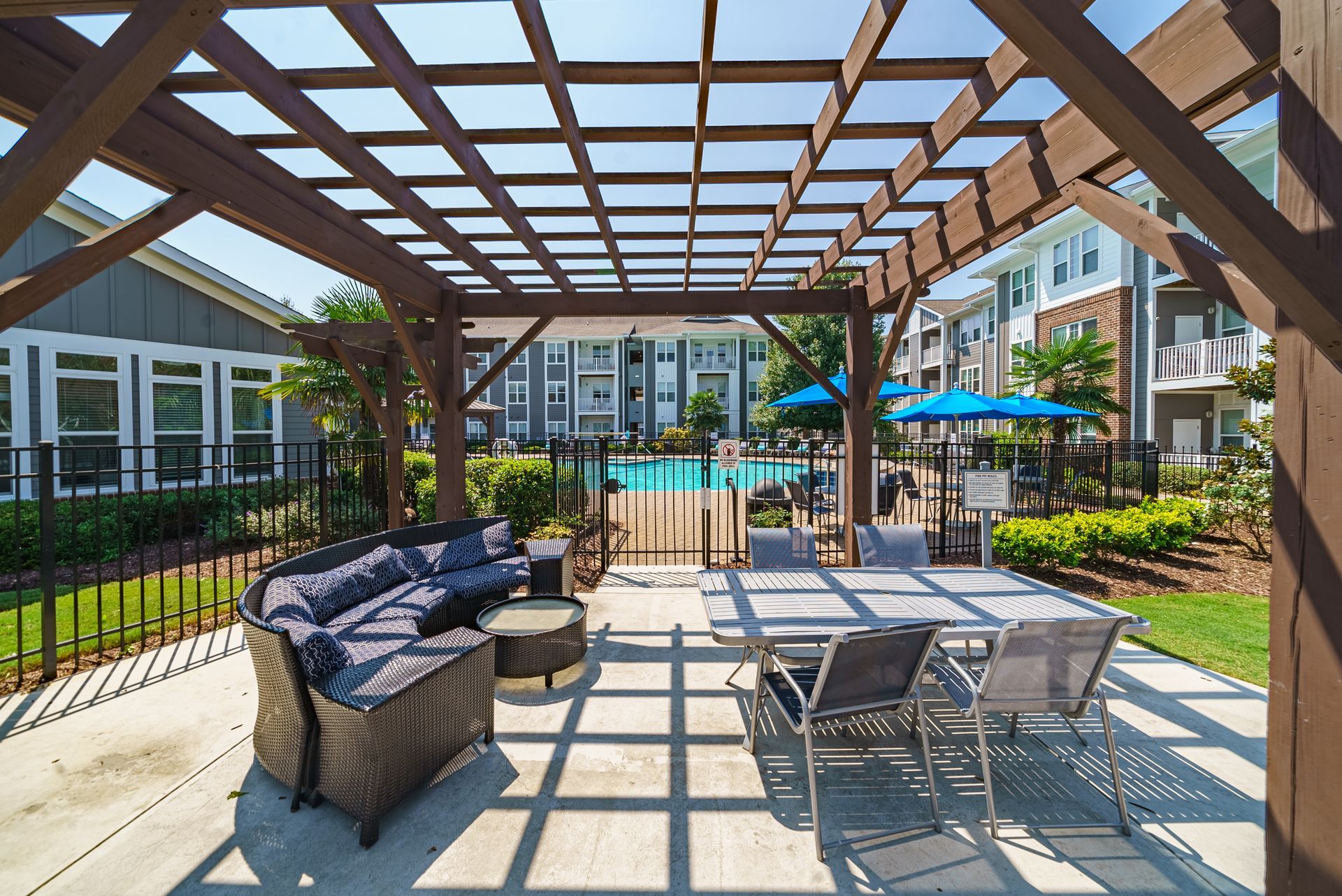 Patio seating under a wooden pergola beside a swimming pool and apartment buildings at Willows at Fort Mill apartments for rent in SC.