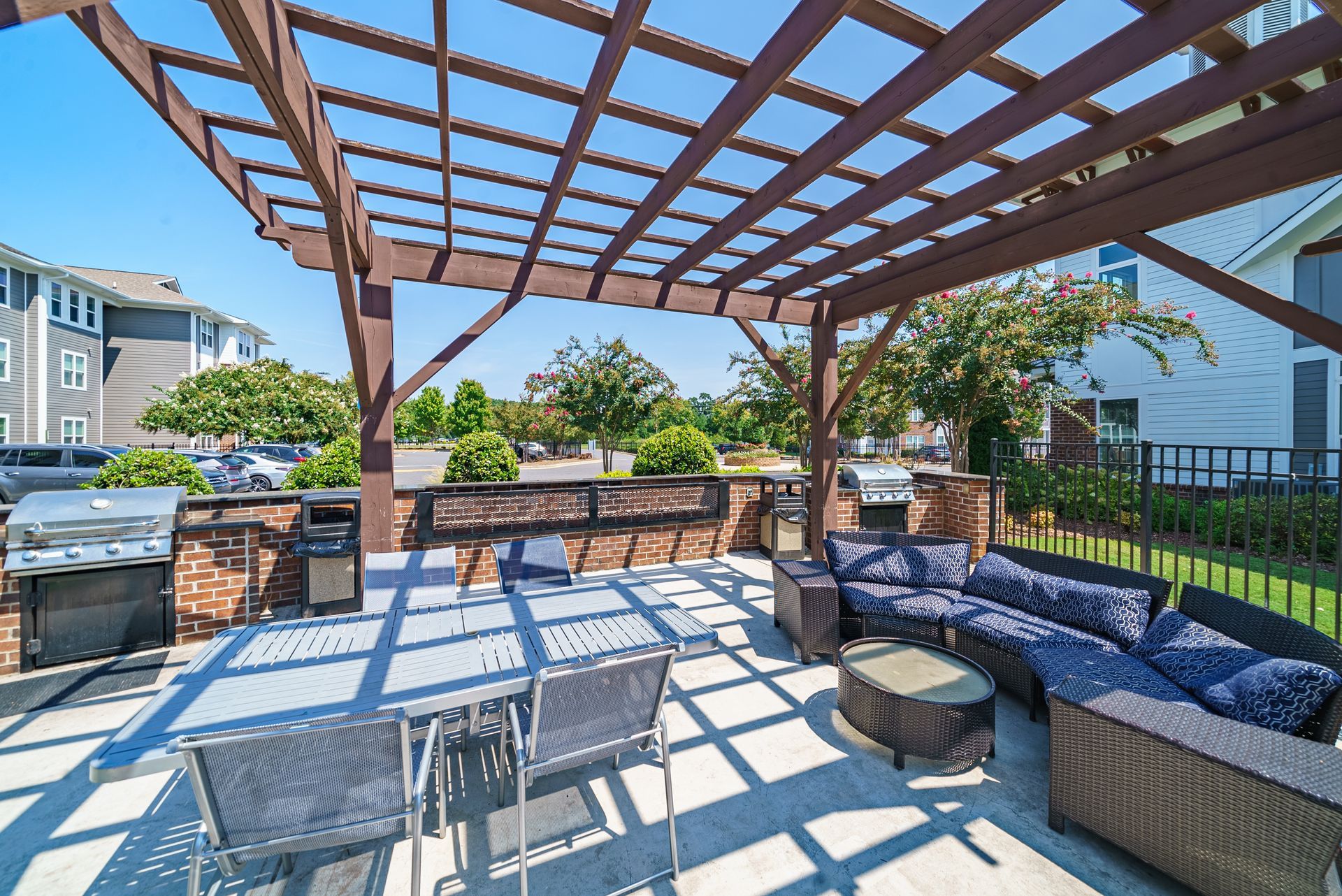 Patio with wooden pergola, outdoor seating, fire pit, and grill in a sunny backyard at Willows at Fort Mill apartments for rent in SC.