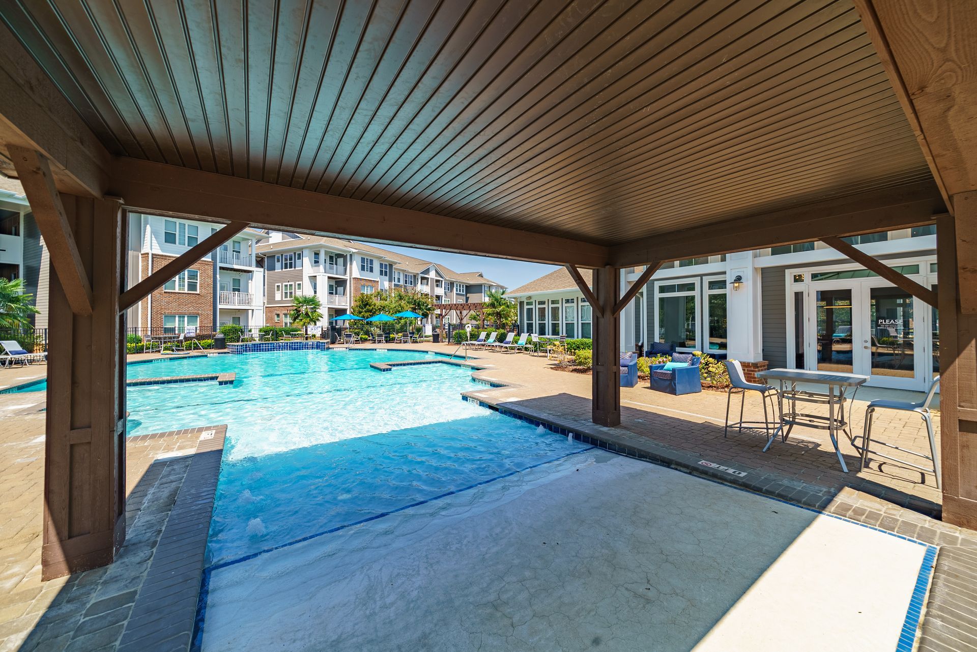 Covered poolside patio with lounge chairs and a resort-style swimming pool in the background at Willows at Fort Mill apartments for rent in SC.