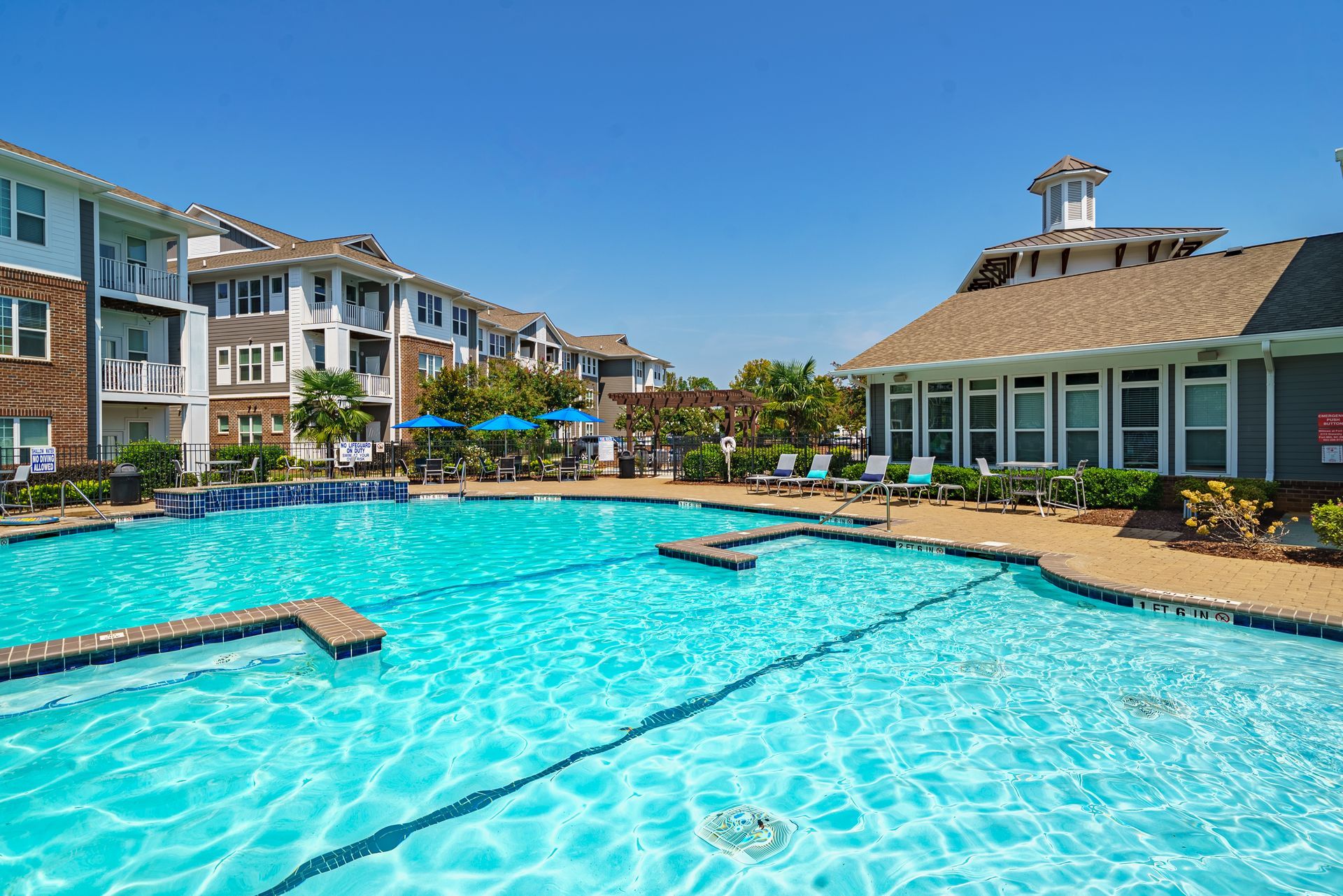 Resort-style swimming pool with turquoise water beside apartment buildings and a clubhouse under a blue sky at Willows at Fort Mill apartments for rent in SC.