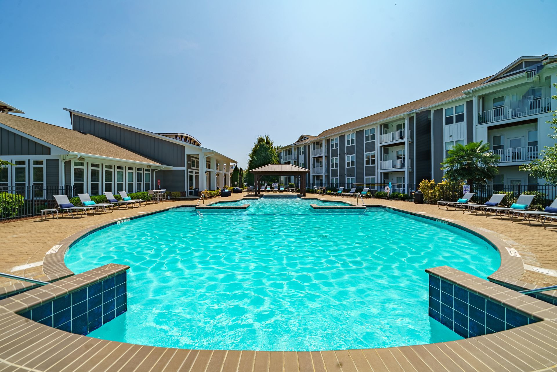 Courtyard resort pool with turquoise water, tan deck, and multi-story buildings under a clear blue sky at Willows at Fort Mill apartments for rent in SC.