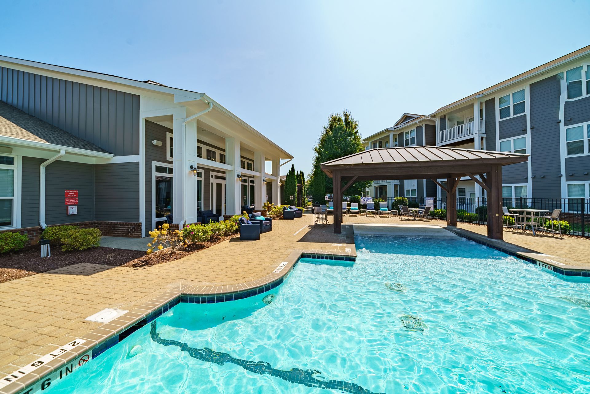 Pool area with buildings, a pergola, tables, and a clear blue sky at Willows at Fort Mill, offers apartments in Fort Mill, SC.