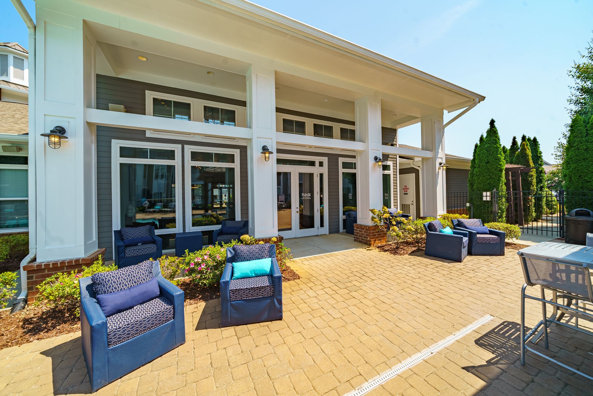 Patio with blue lounge chairs outside a modern white house with large windows and sliding doors at Willows at Fort Mill apartments for rent in SC.