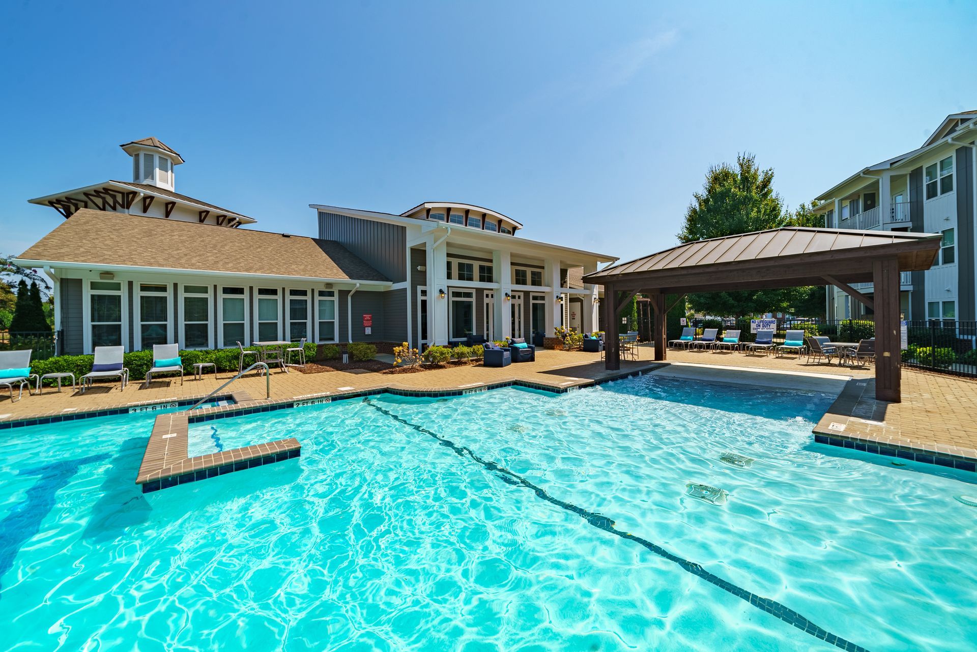 Luxury backyard pool beside a modern home, with turquoise water and a covered patio under a clear sky at Willows at Fort Mill apartments for rent in SC.