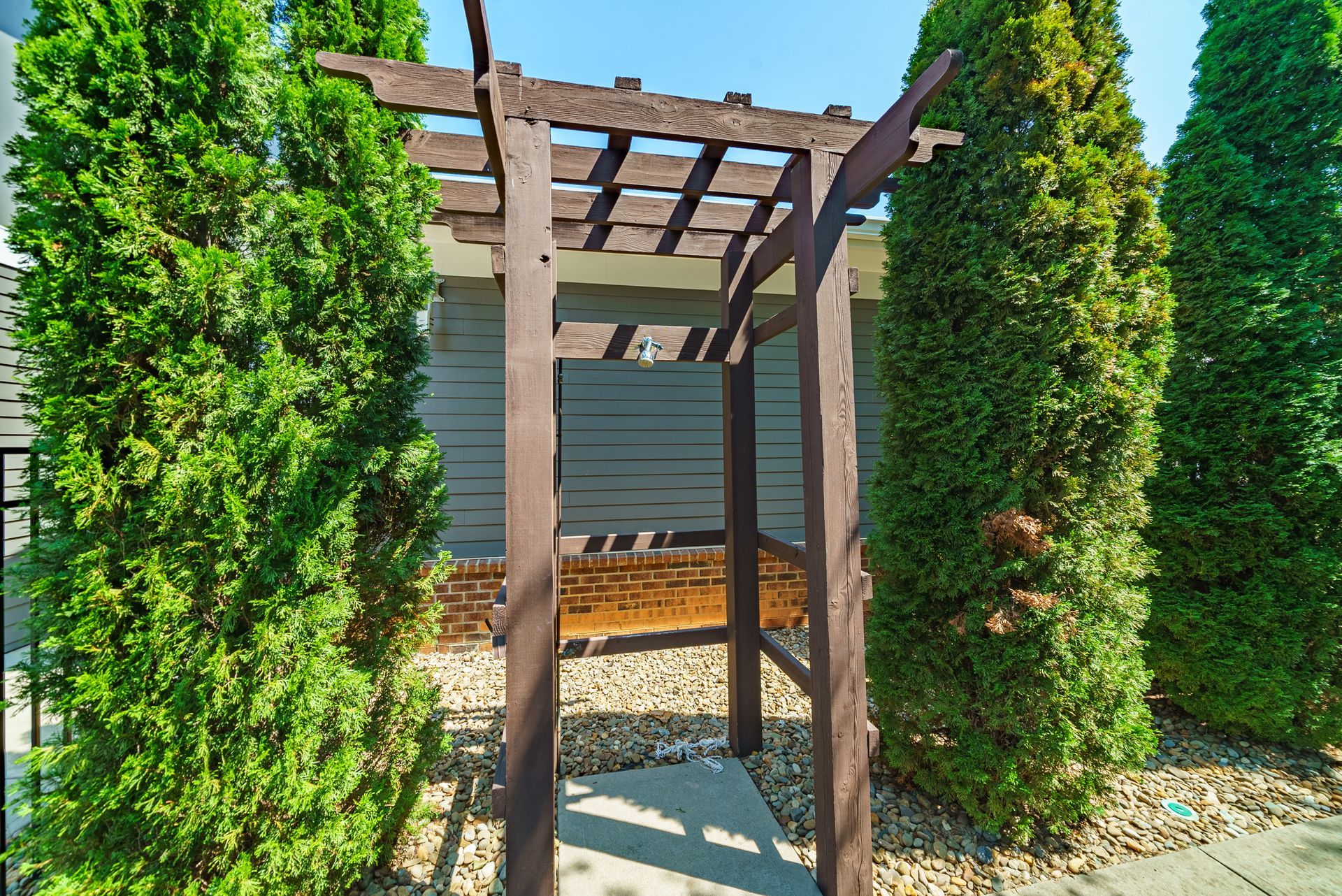 Wooden garden pergola framed by two tall green shrubs with a gravel path below at Willows at Fort Mill apartments for rent in SC.