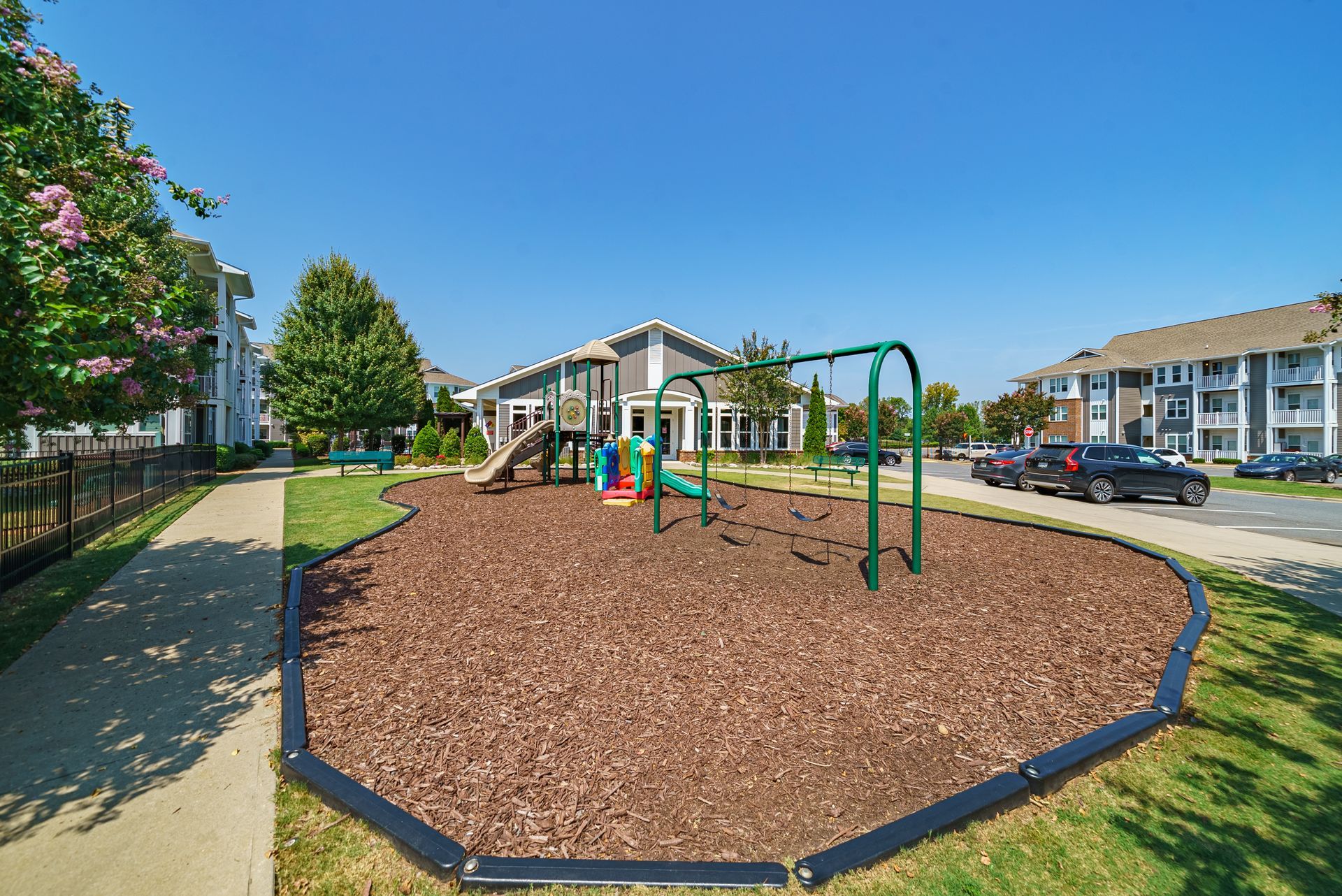 Apartment playground with swings and slide, bordered by mulch and grass on a sunny day at Willows at Fort Mill apartments for rent in SC.