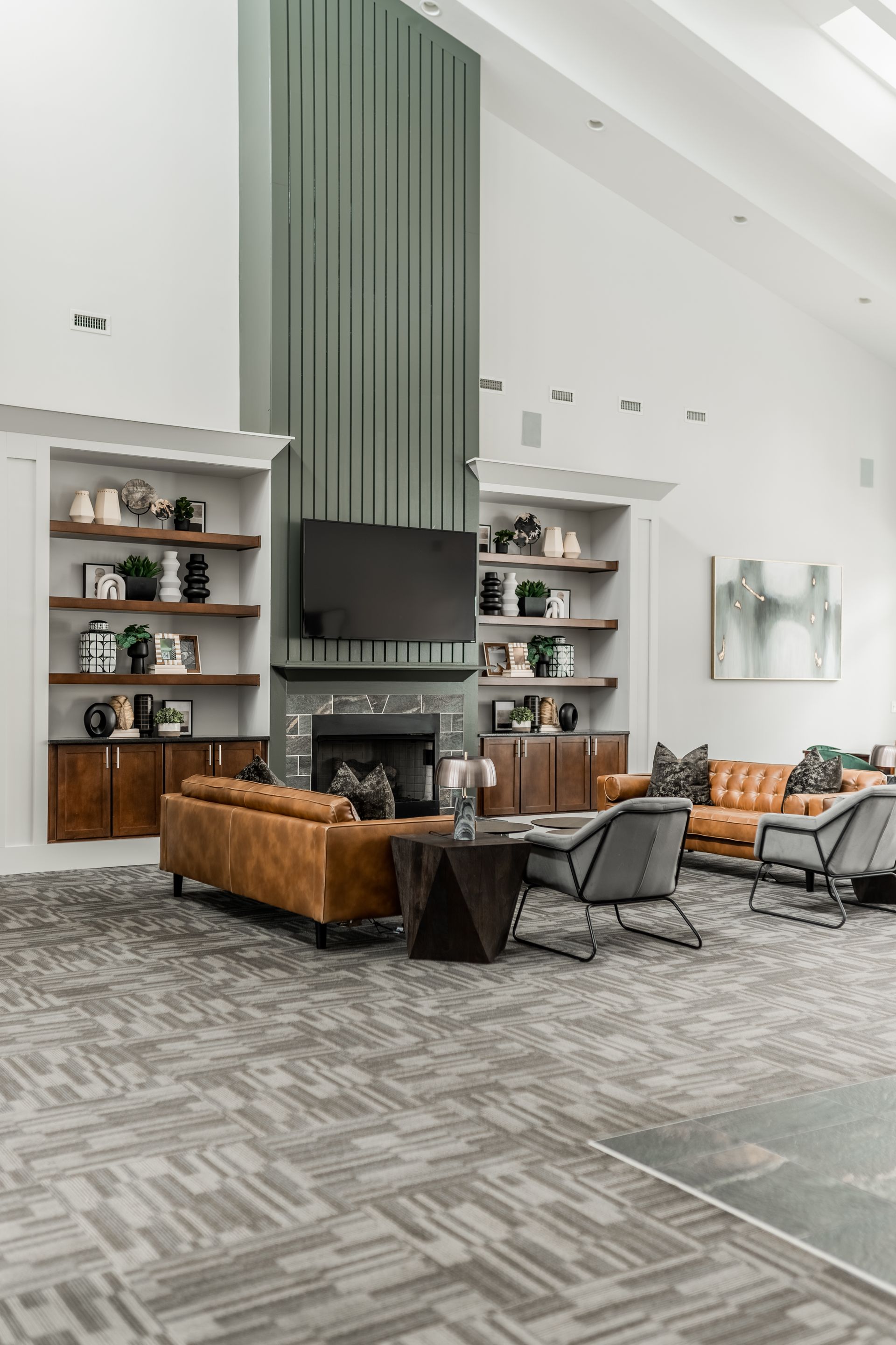 Modern lounge with tall fireplace, built-in shelves, tan leather sofas, and patterned gray carpet at Willows at Fort Mill apartments for rent in SC.