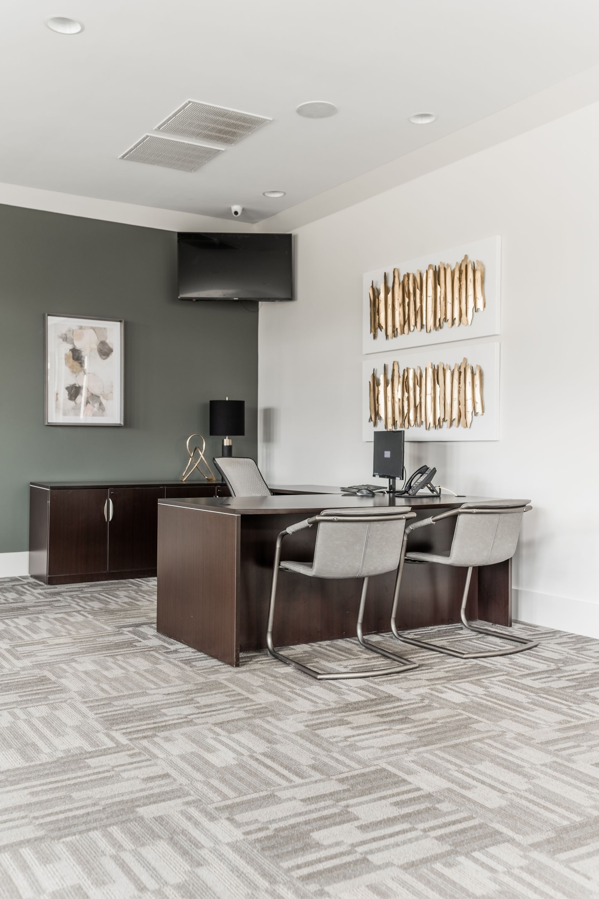 Modern office reception area with a desk, chairs, wall art, and a mounted TV at Willows at Fort Mill apartments for rent in SC.