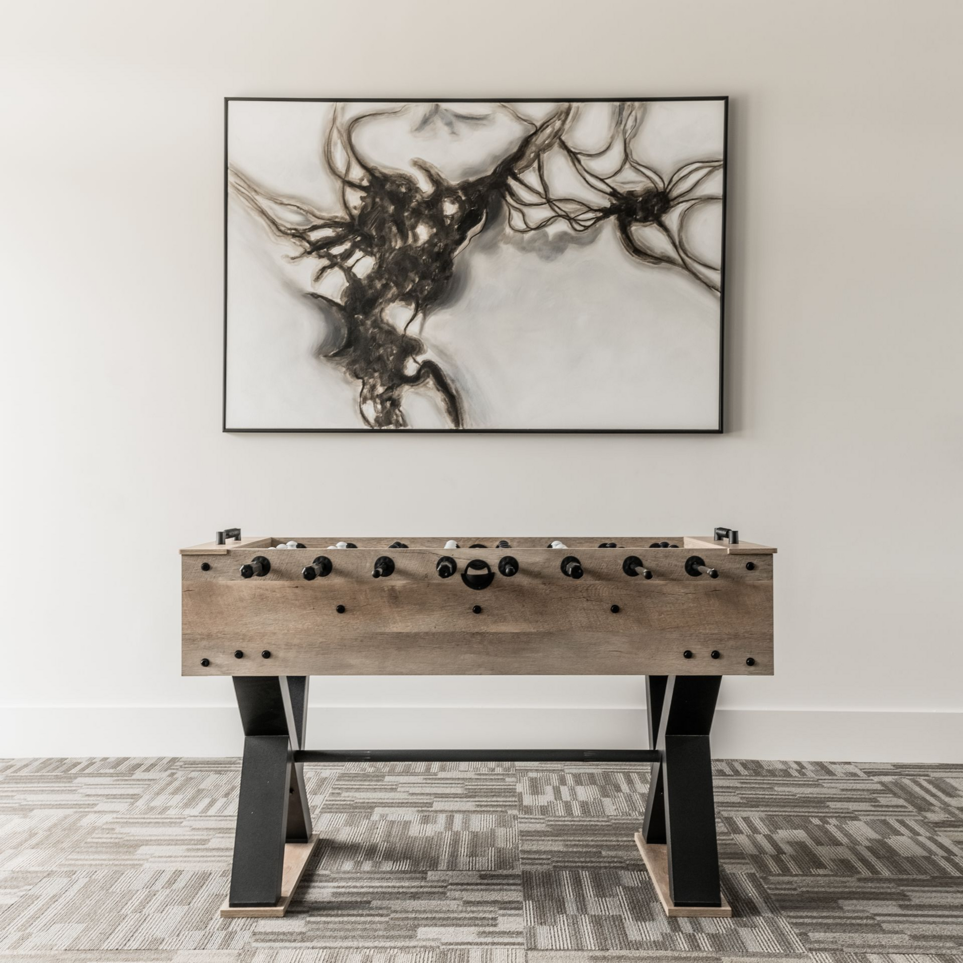 Modern room with a framed abstract black wall artwork above a wooden foosball table at Willows at Fort Mill apartments for rent in SC.