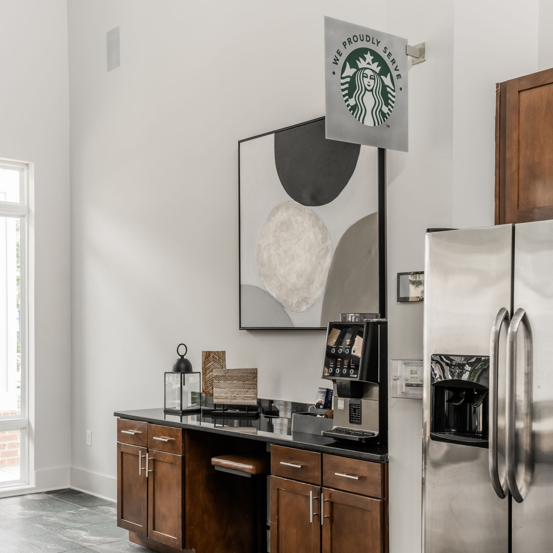 Modern kitchen coffee bar with stainless steel fridge, wooden cabinets, and abstract wall art at Willows at Fort Mill apartments for rent in SC.