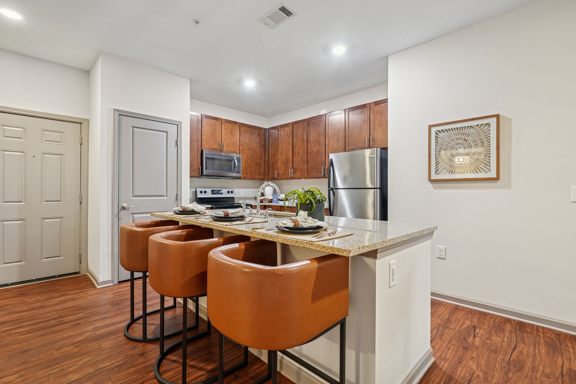 Bright kitchen with granite island, brown bar stools, stainless fridge, and wood cabinets at Willows at Fort Mill apartments for rent in SC.