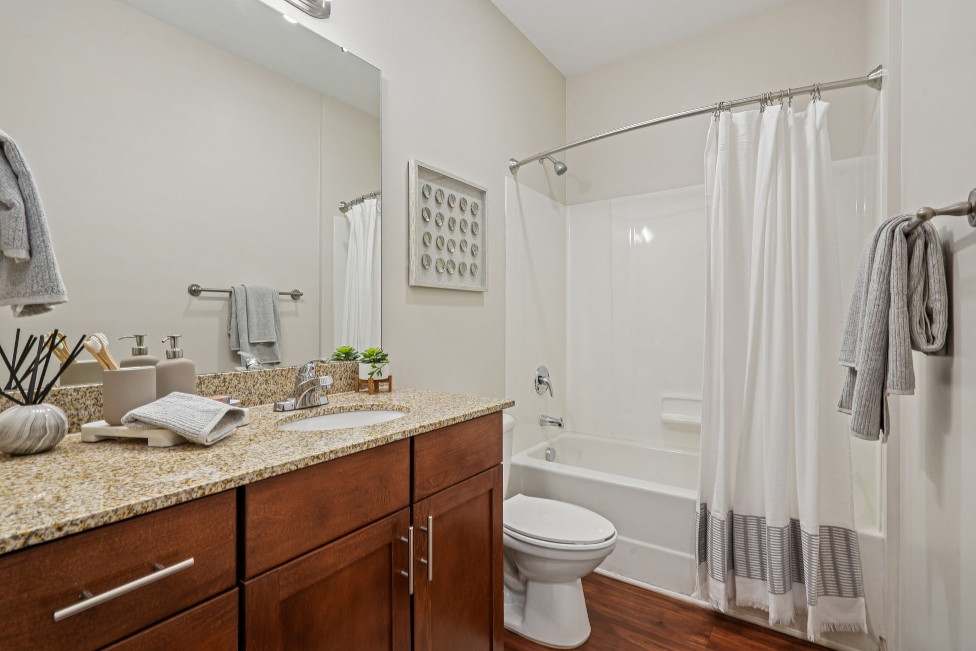 Bathroom with wooden vanity, granite countertop, toilet, and shower with white curtain at Willows at Fort Mill apartments for rent in SC.