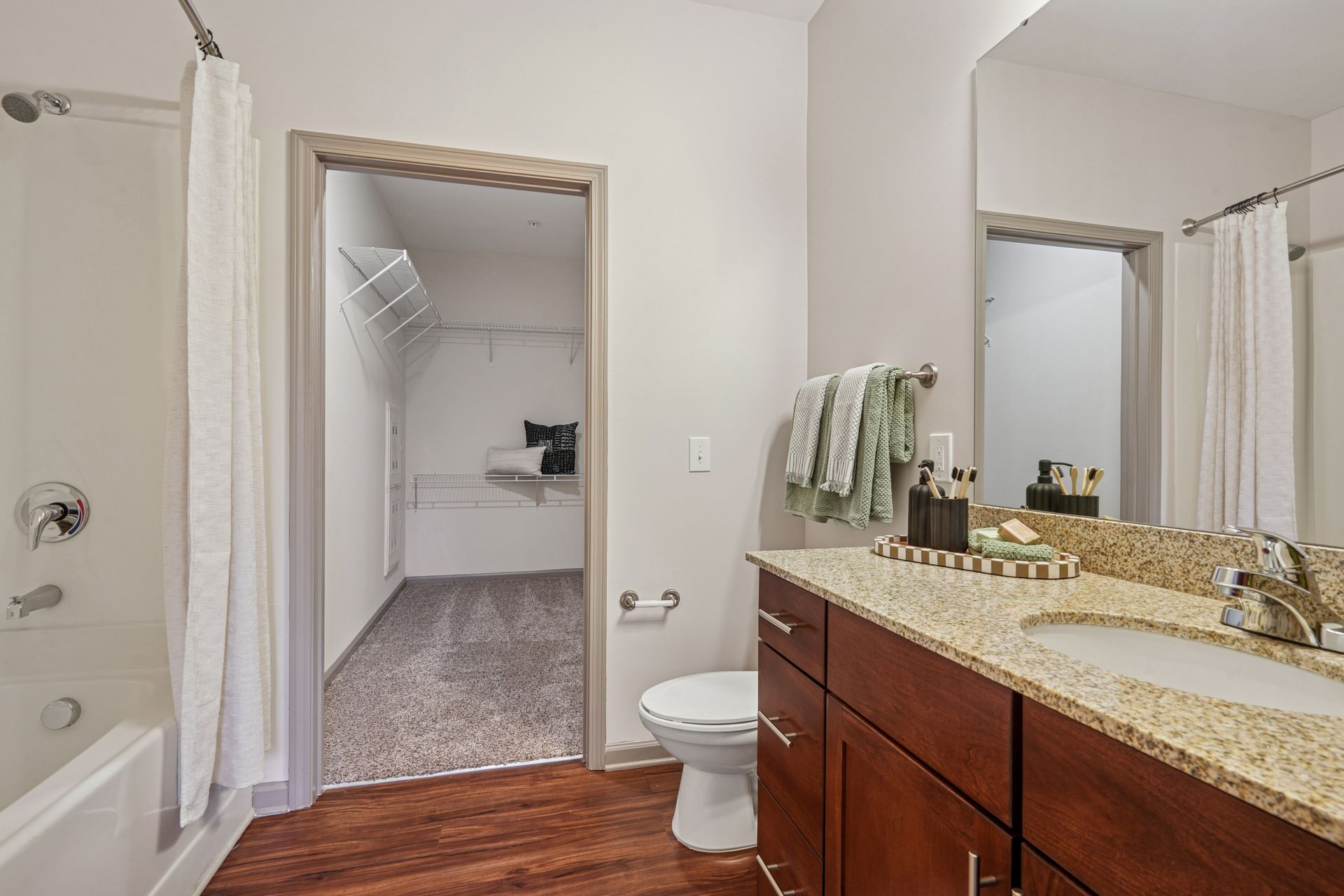 Bathroom with wood vanity, beige countertop, toilet, and open doorway to a carpeted closet or dressing area at Willows at Fort Mill apartments for rent in SC.