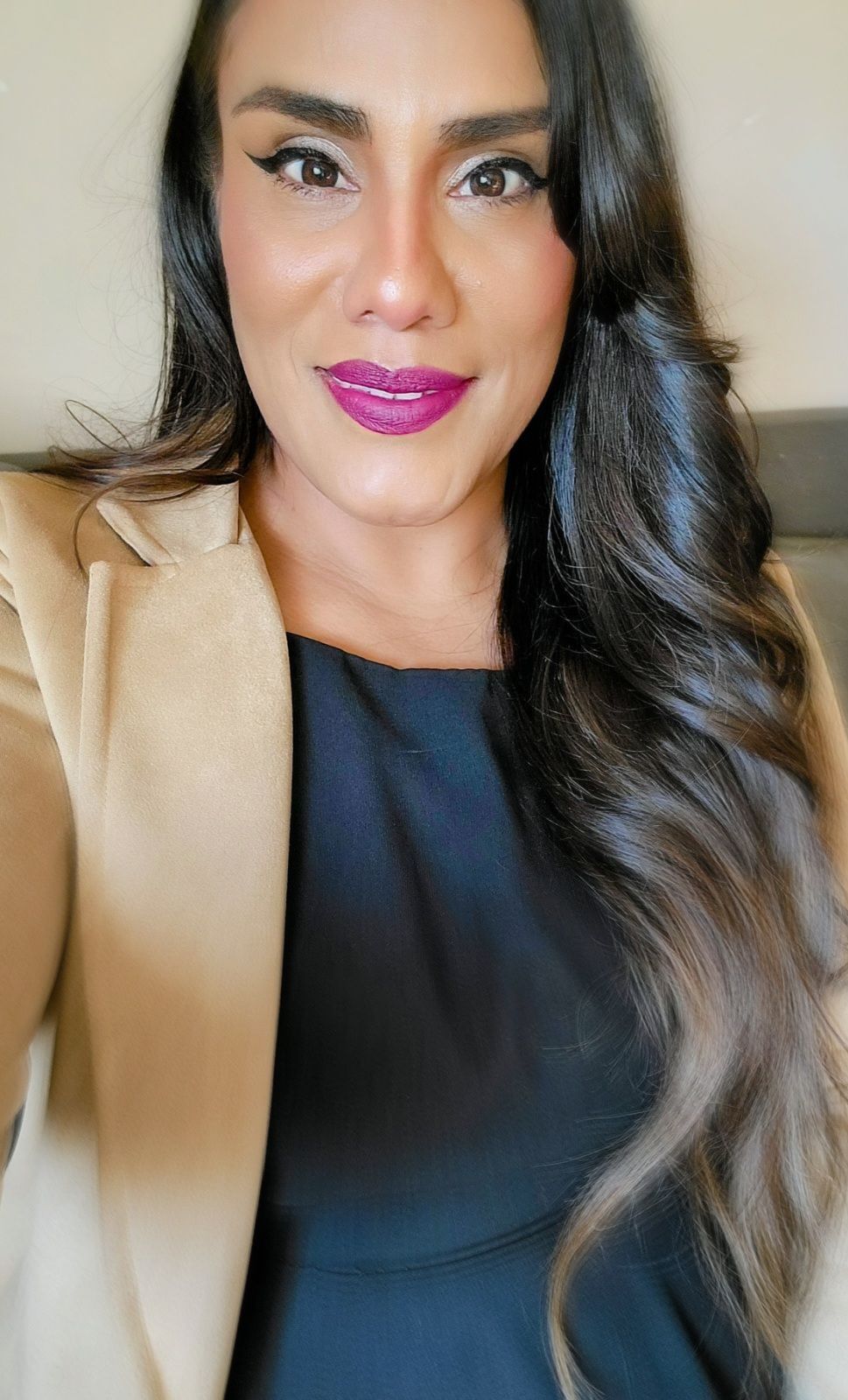 A woman wearing a brown hat with feathers on it is smiling.