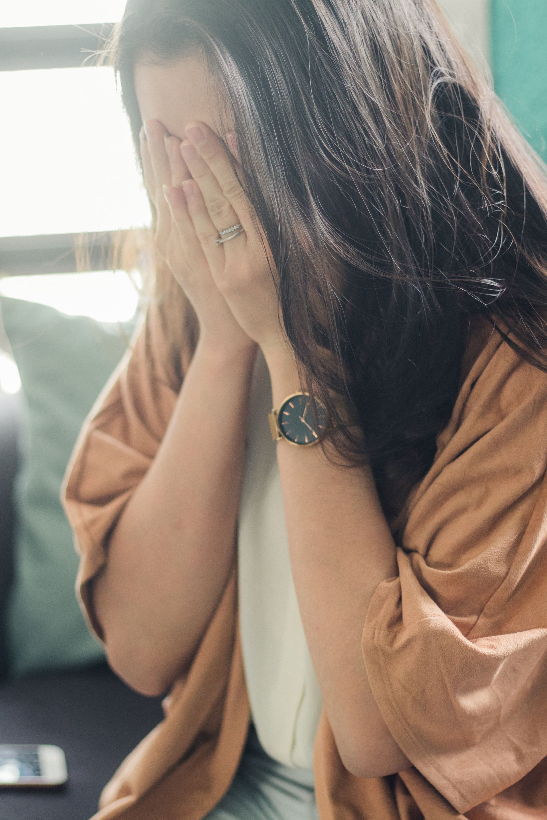 A woman is covering her face with her hands while wearing a watch.