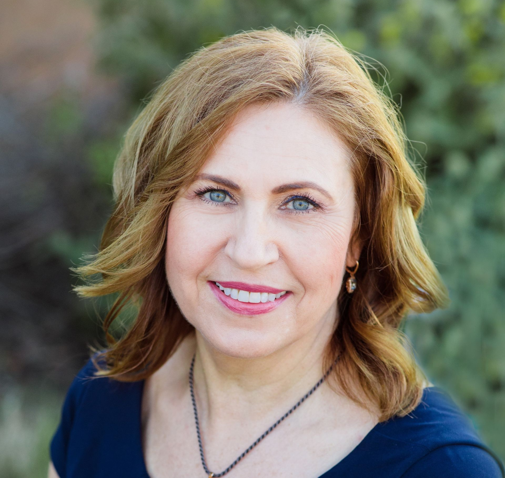 A woman wearing a green shirt and a gold necklace is smiling for the camera.
