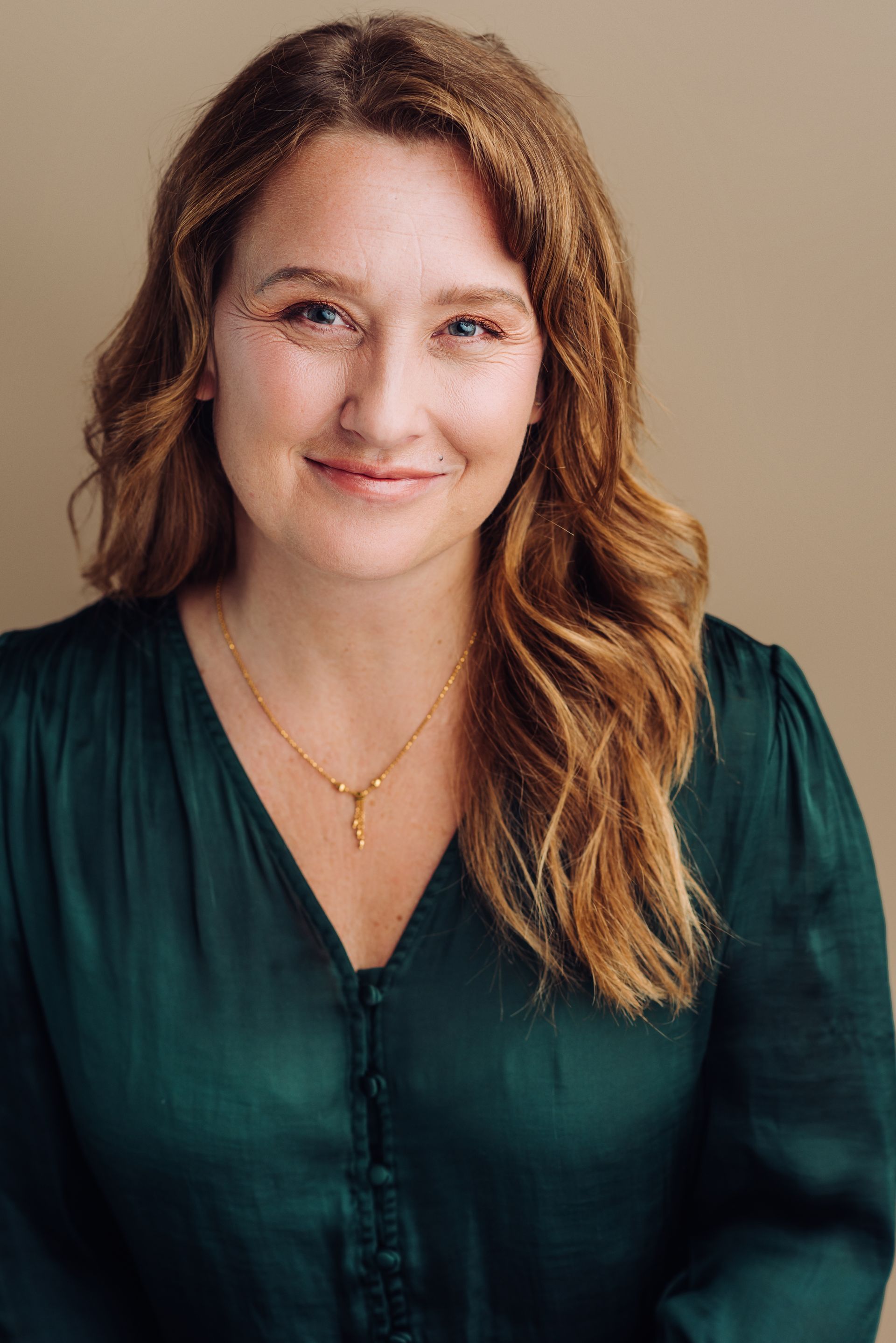 A woman wearing a green shirt and a gold necklace is smiling for the camera.