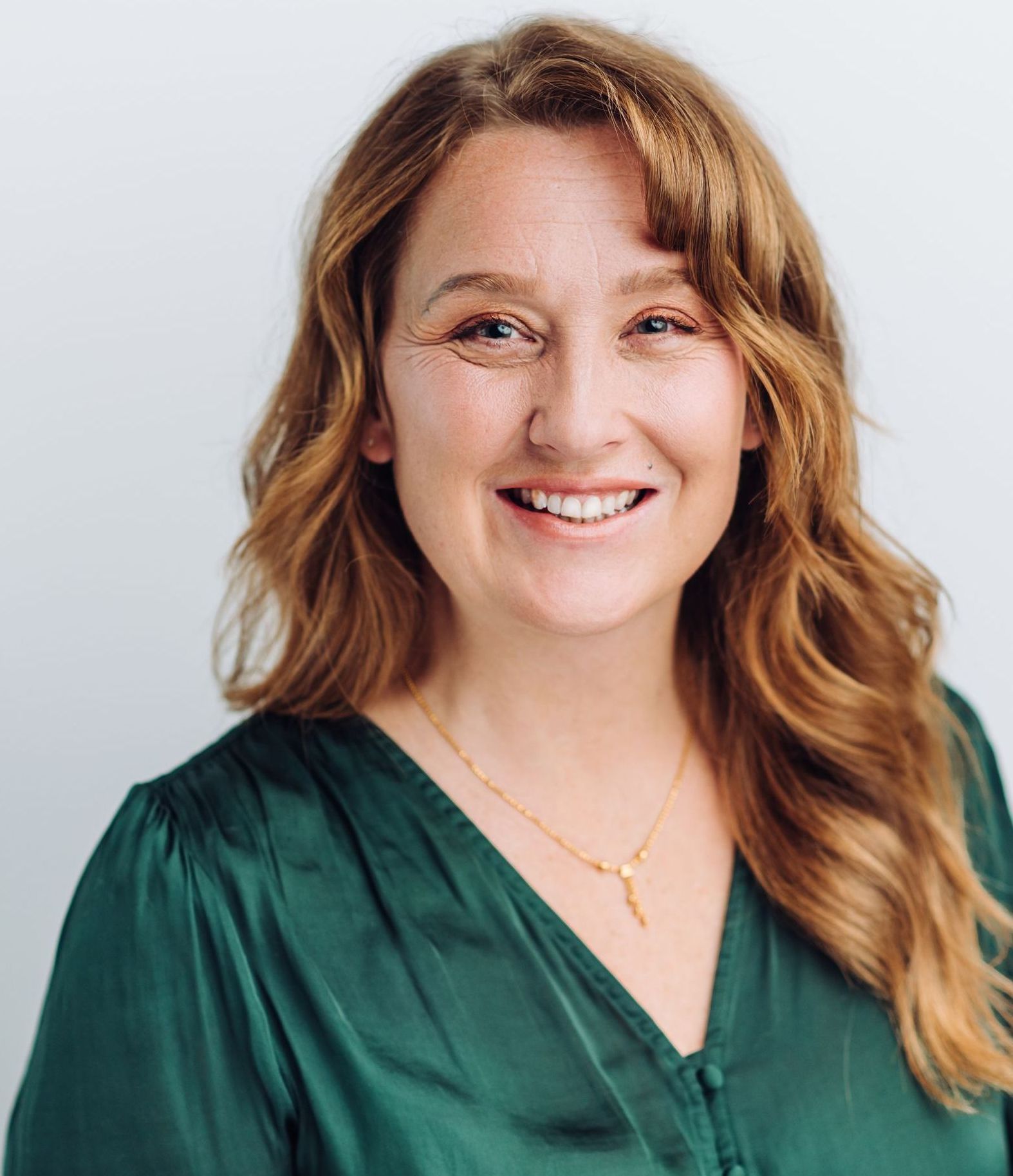 A woman wearing a green shirt and a gold necklace is smiling for the camera.