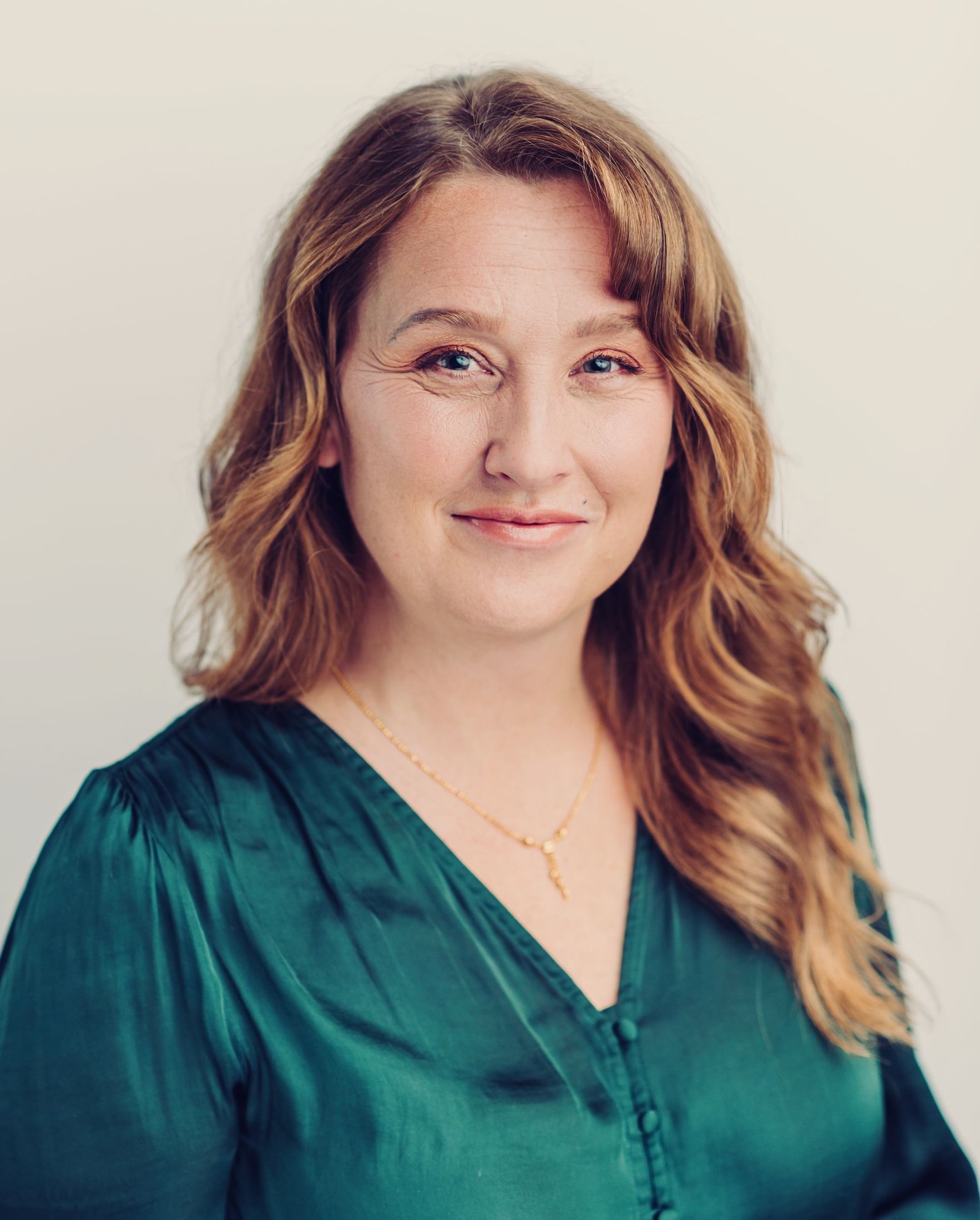 The woman is wearing a green shirt and a gold necklace.