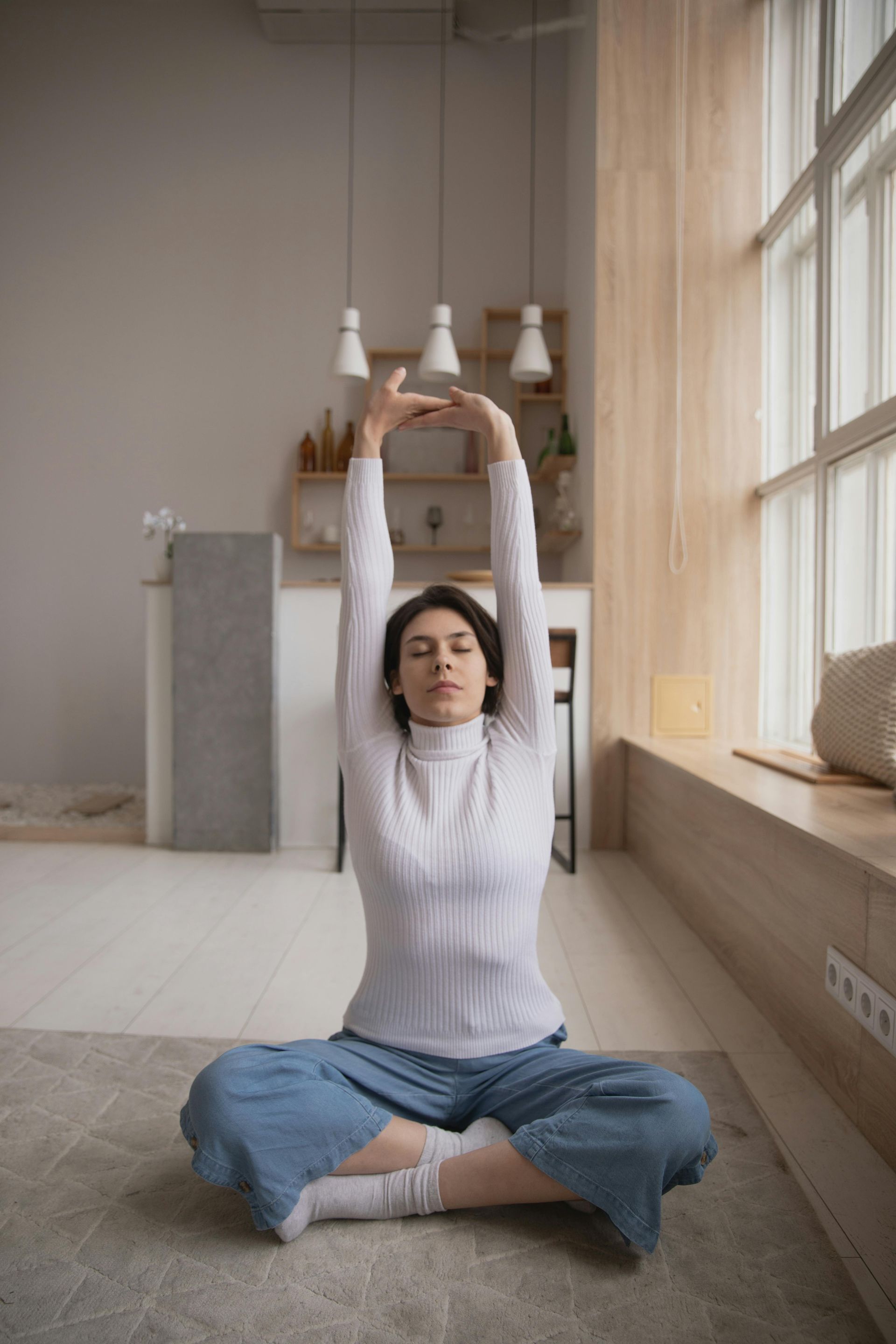 A woman is sitting on the floor in a lotus position with her arms outstretched.