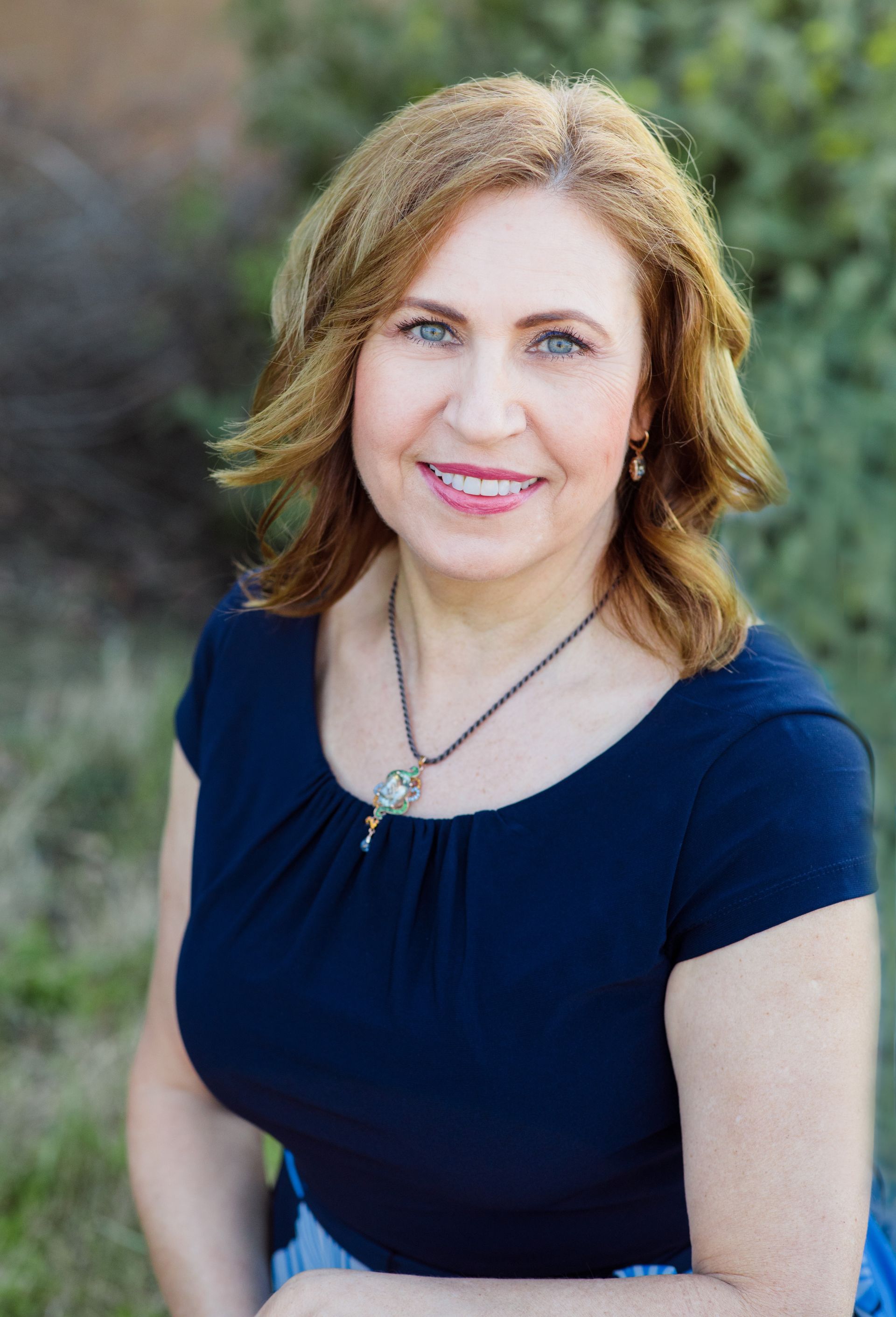 A woman wearing a green shirt and a gold necklace is smiling for the camera.