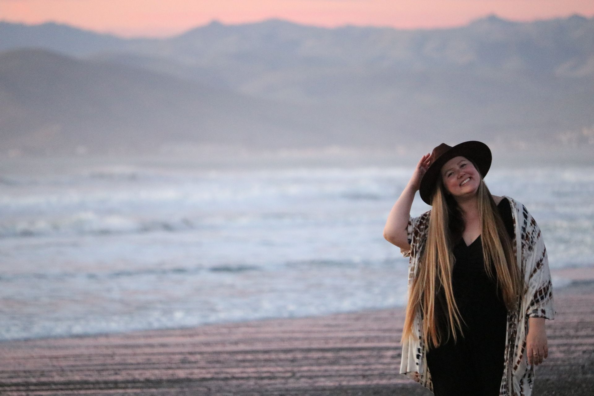 A woman wearing a hat is standing on a beach.