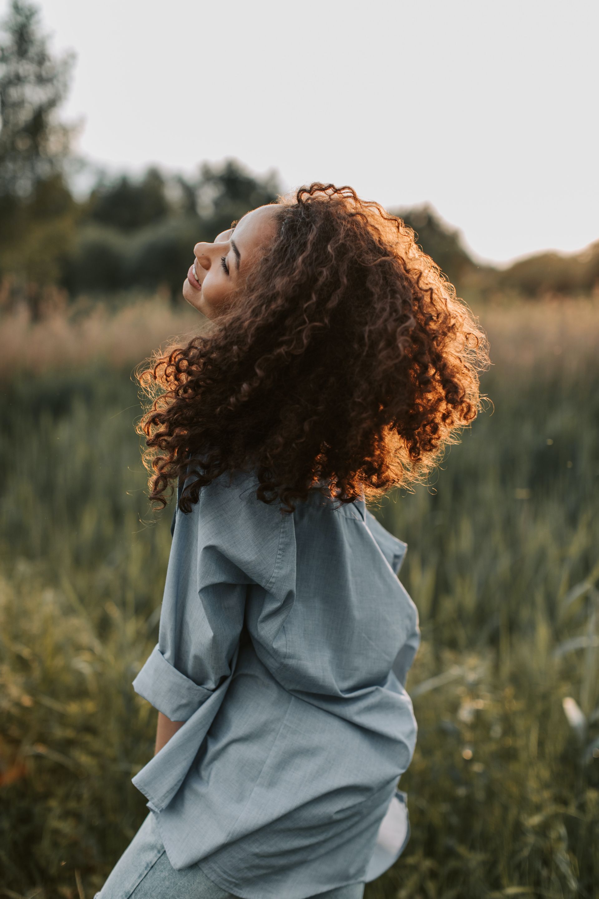 A woman with curly hair is standing in a field with her head up.