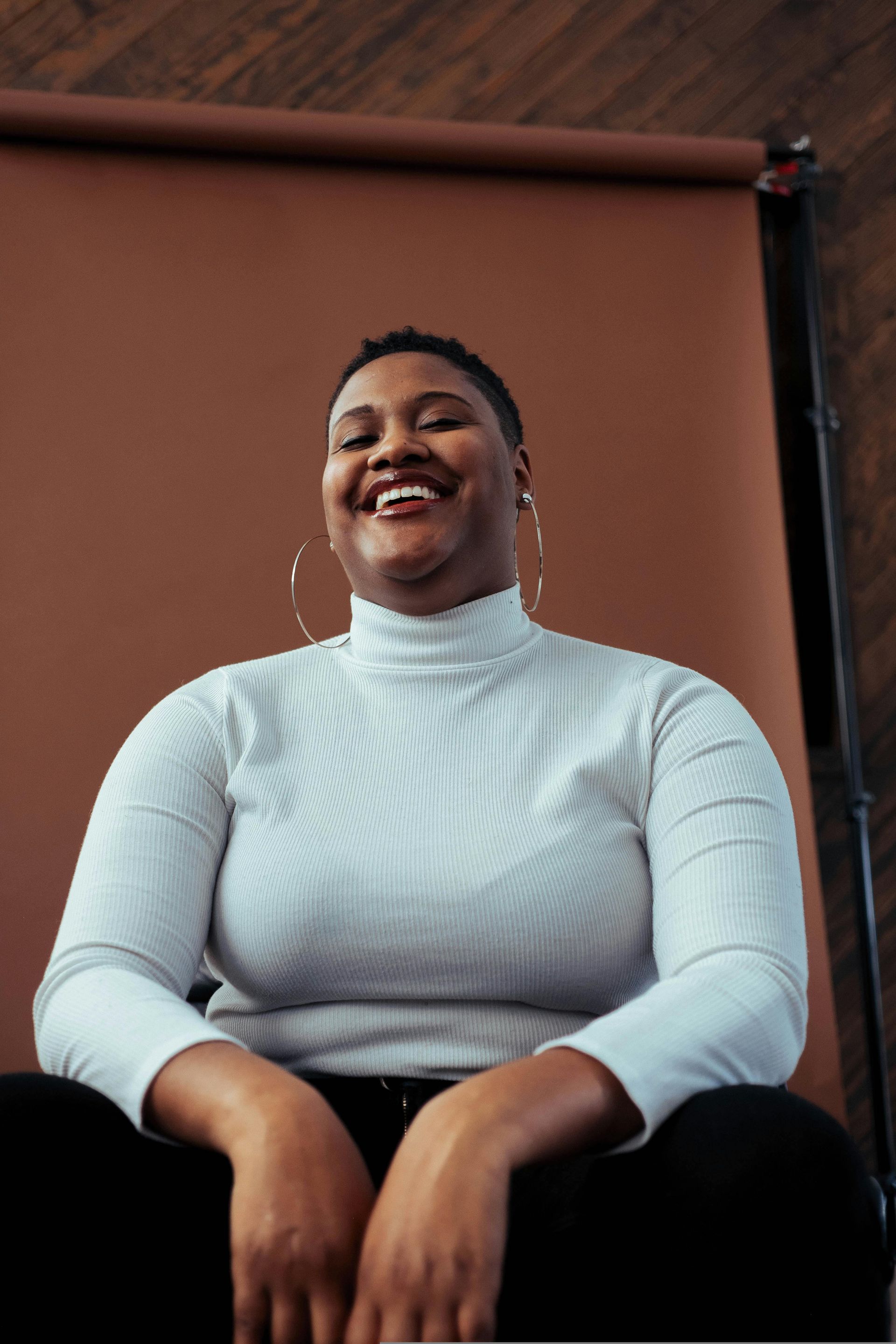 A woman in a white turtleneck is smiling while sitting down.