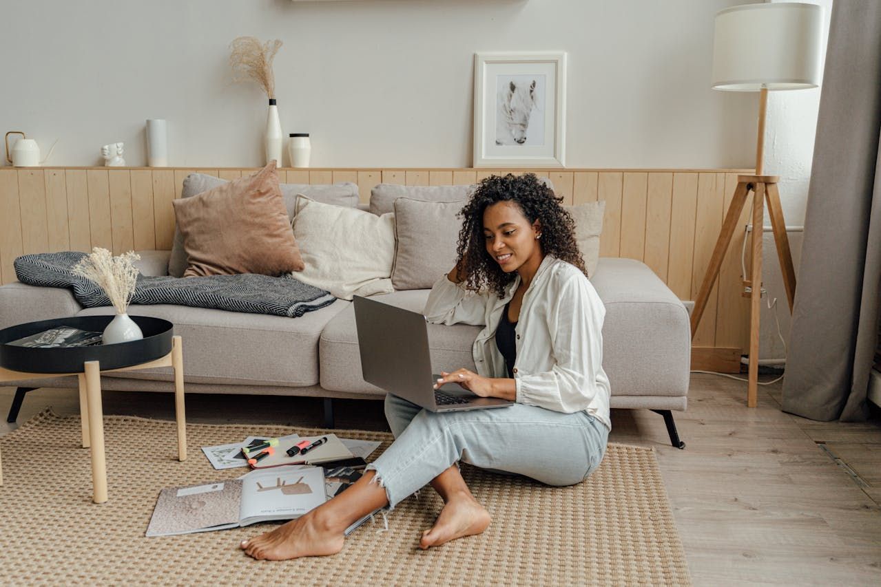 A woman is sitting on the floor in a living room using a laptop computer.
