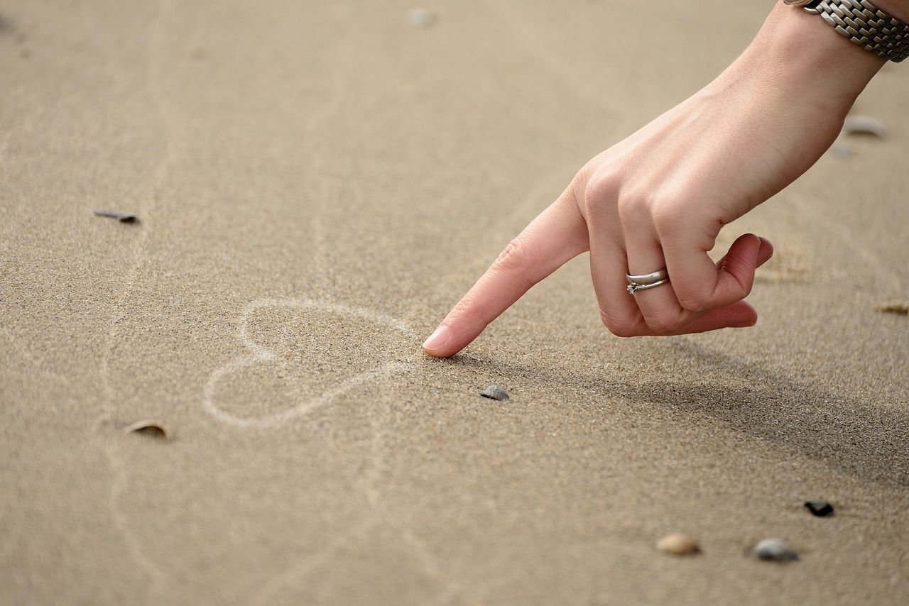 A woman is pointing at a heart drawn in the sand.