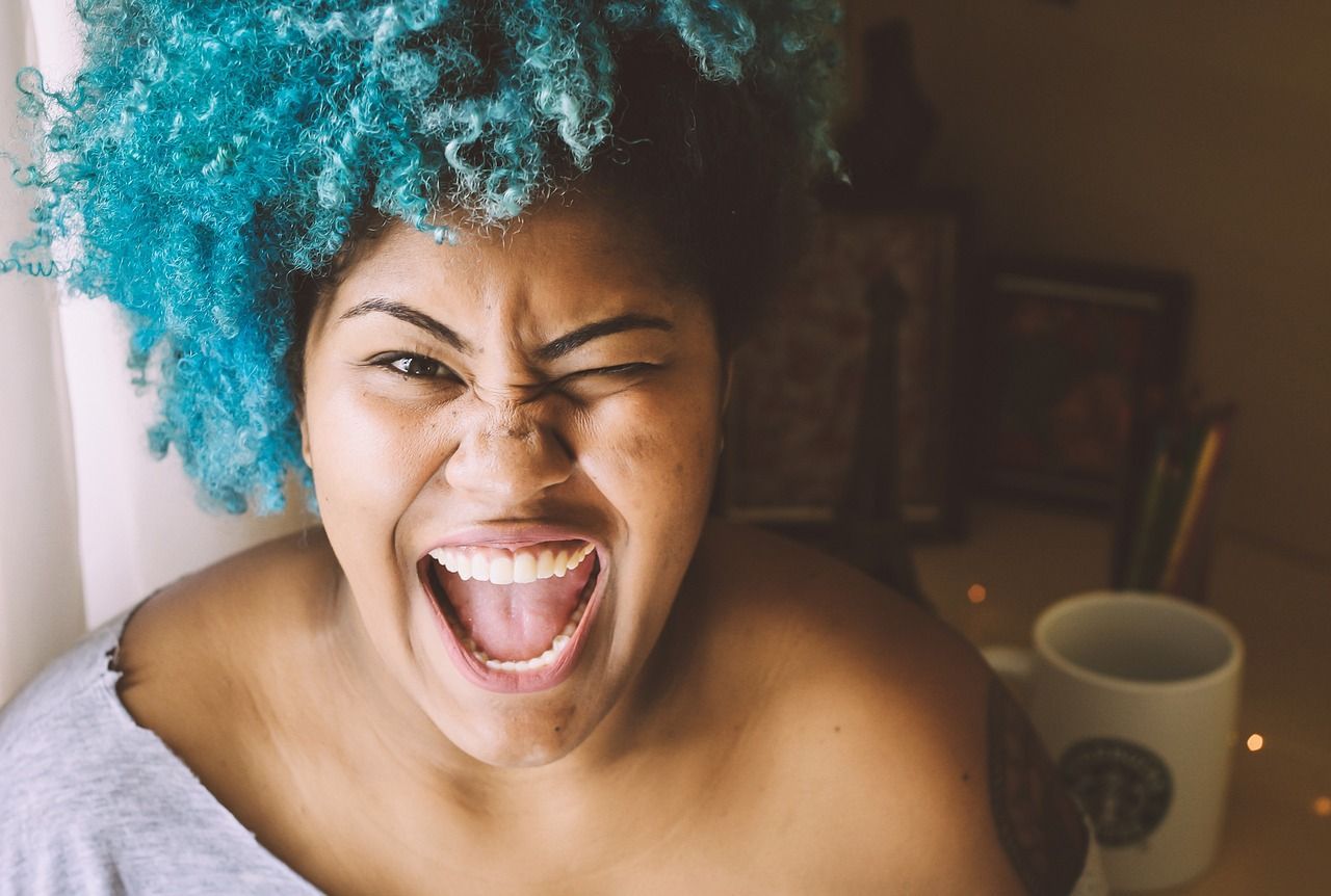 A woman with blue hair is making a funny face with her mouth open.