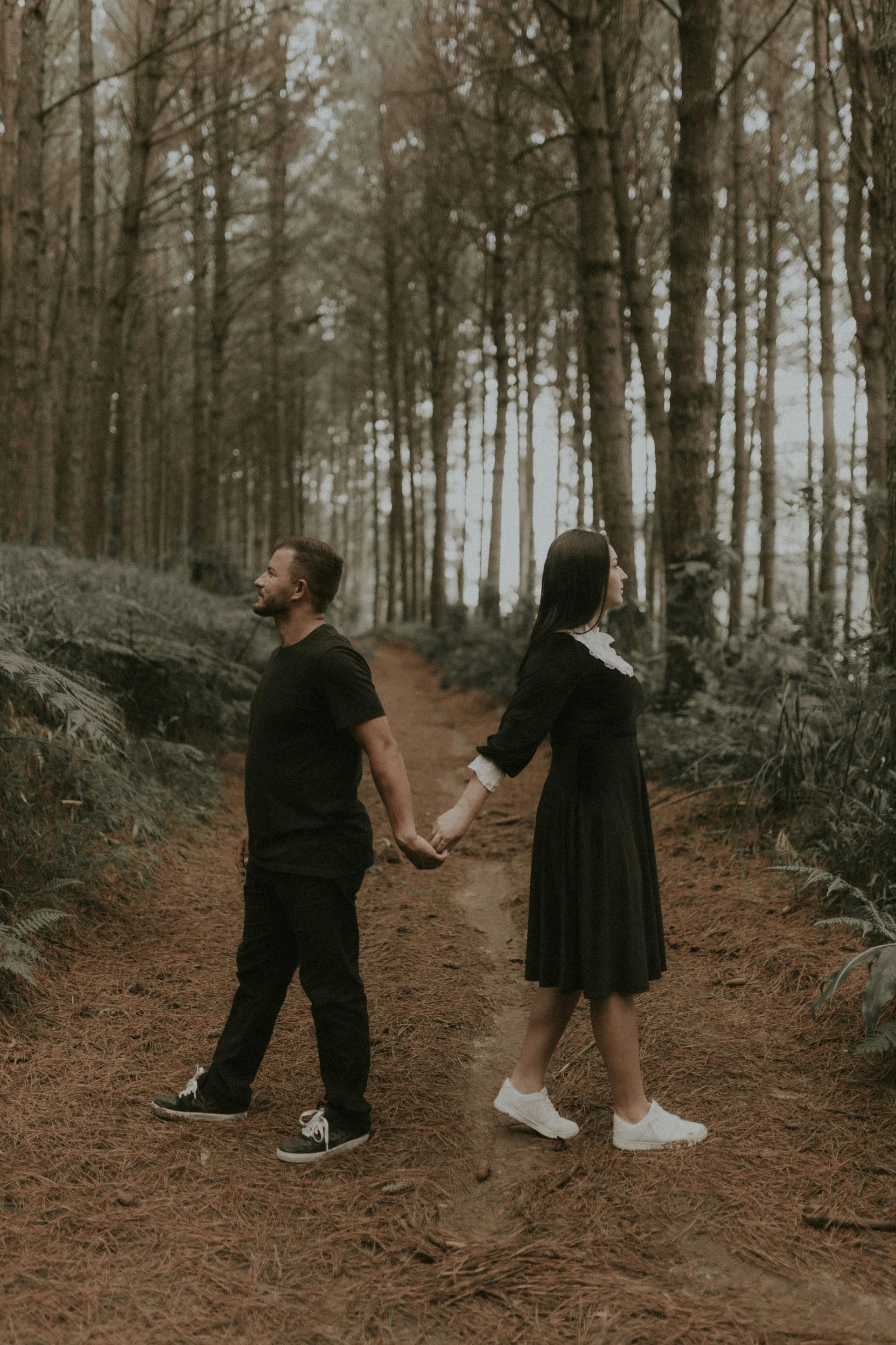 A man and a woman are holding hands in the woods.