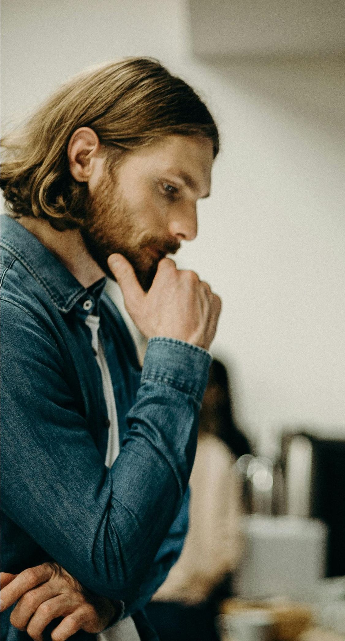 A man with a beard is thinking with his hand on his chin.