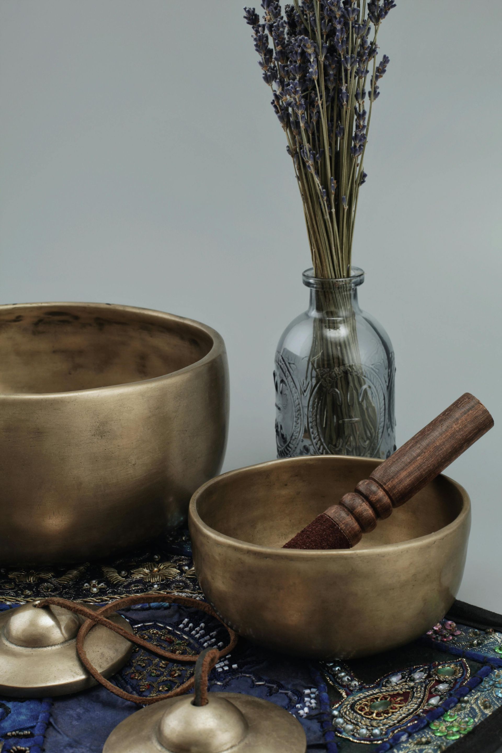 Two brass bowls with a wooden handle and a vase of lavender flowers on a table.