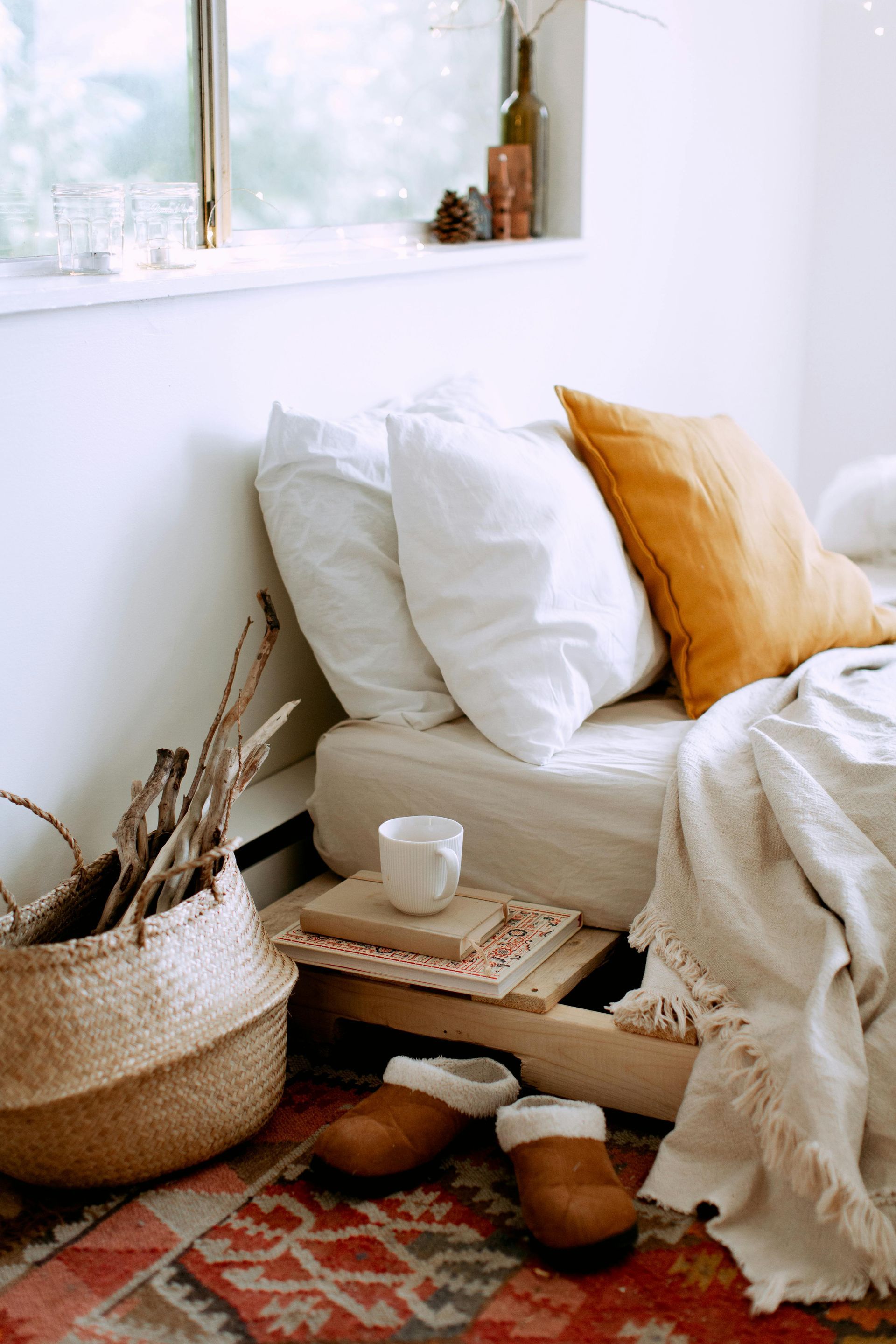 A bedroom with a bed , slippers , a basket of logs , and a rug.