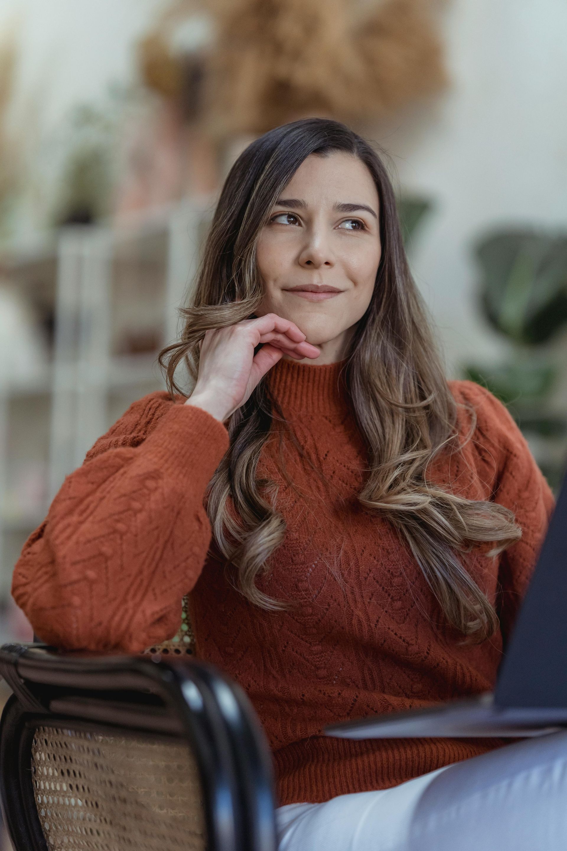 A woman in an orange sweater is sitting at a table with a laptop.