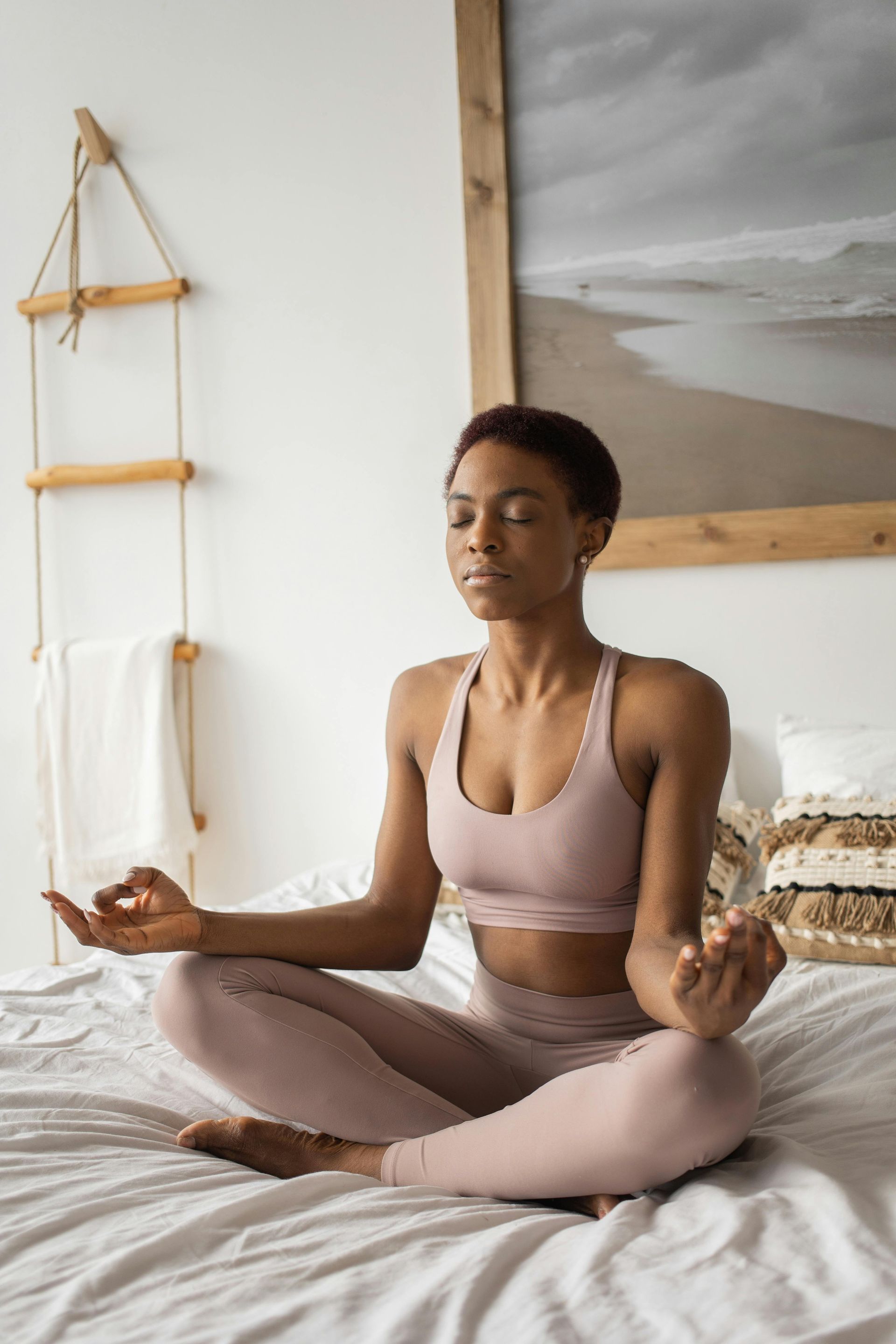 A woman is sitting on a bed in a lotus position meditating.
